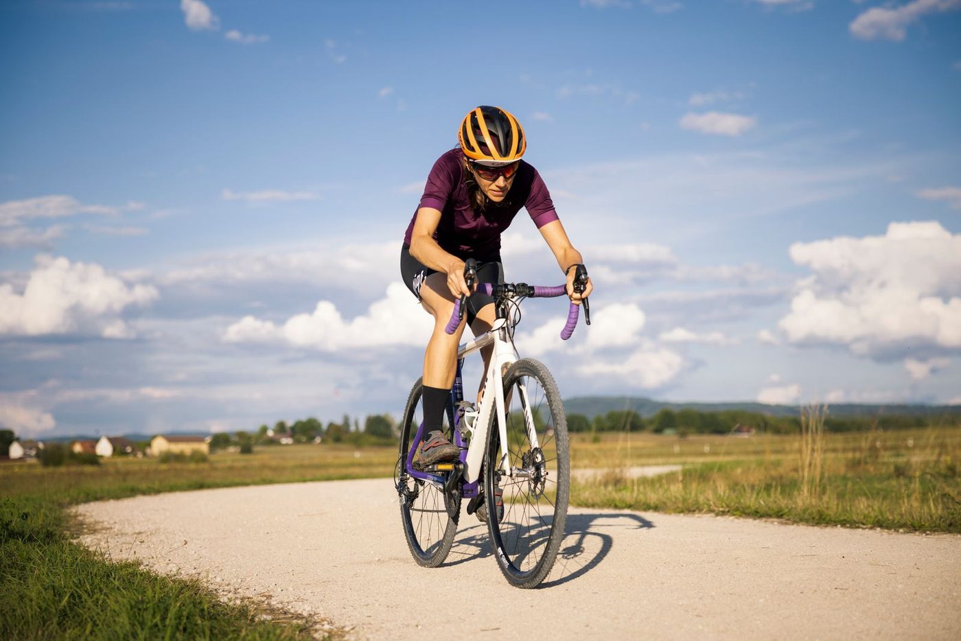 A cyclist riding a loaded gravel bike along an open dirt road beneath a wide sky of broken cloud.
