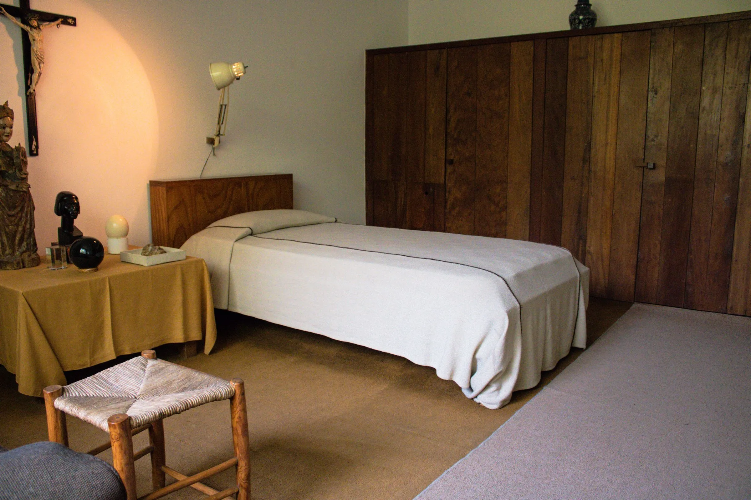A bedroom in warm neutral tones with low timber furniture and simple decoration.