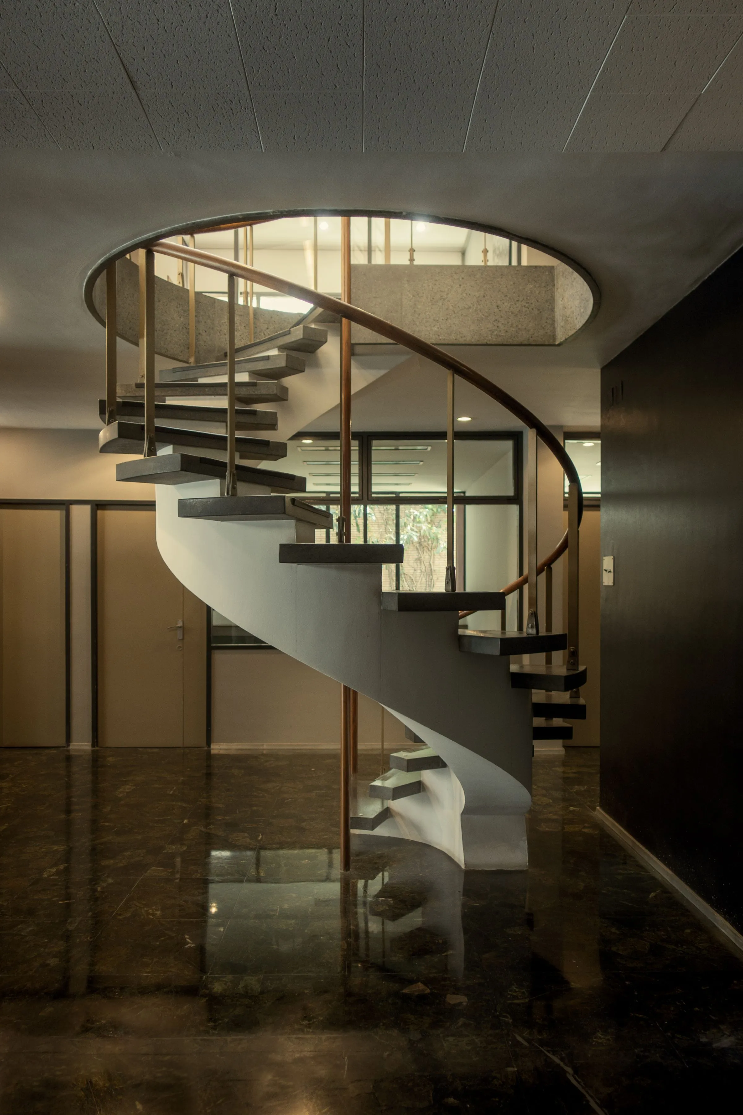 Curved staircase at The Oak House with a dark metal balustrade and polished floor below.