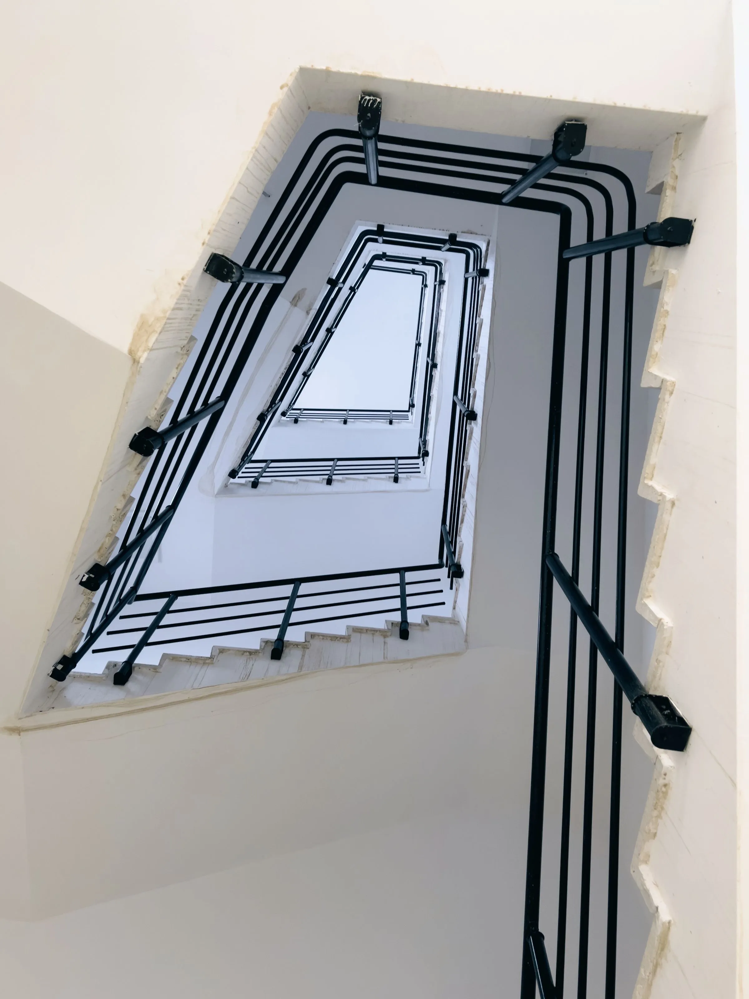 Looking down a modern staircase with a slim black handrail against white walls.