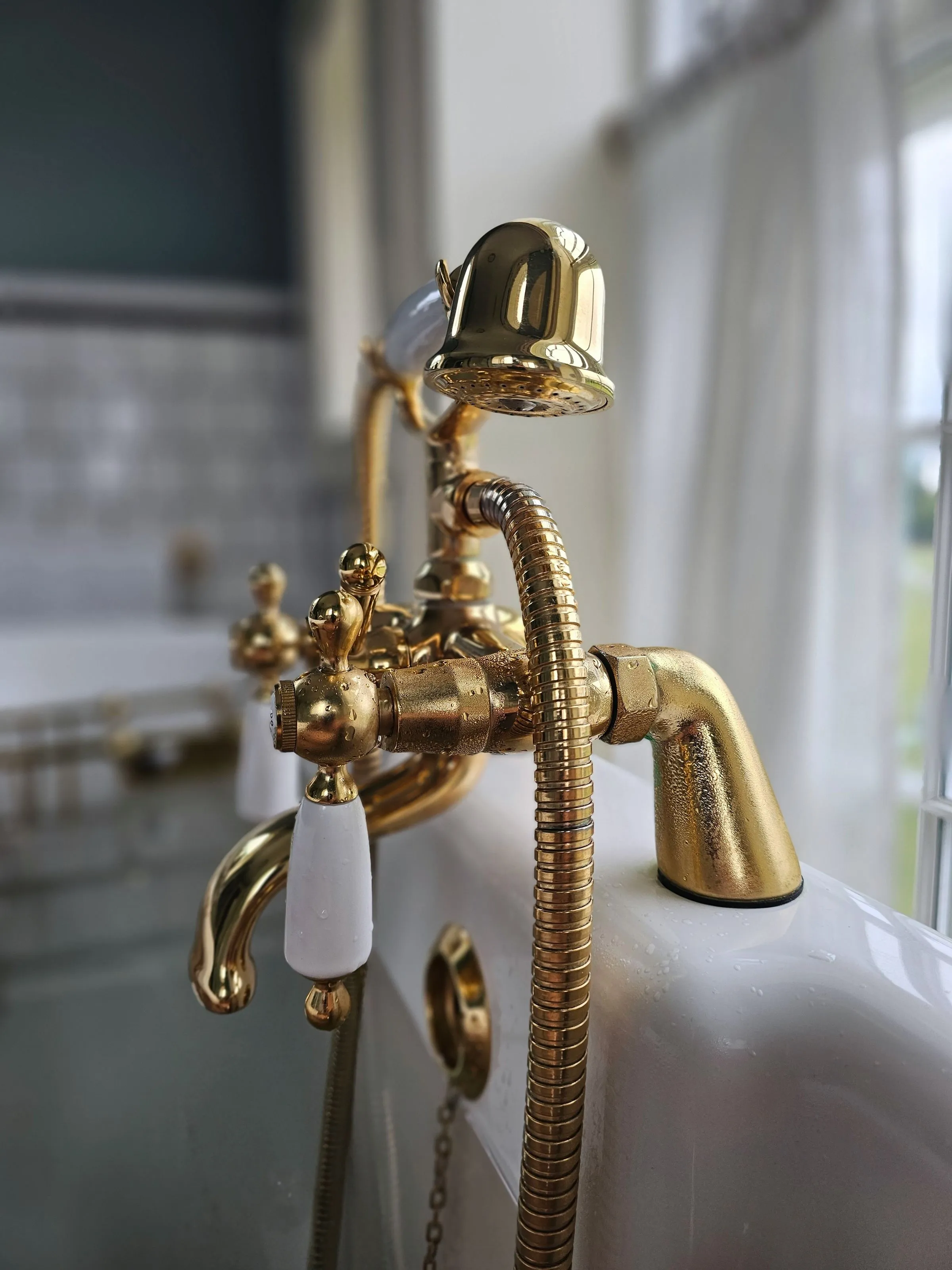 A close view of an aged brass tap against a pale tiled wall.