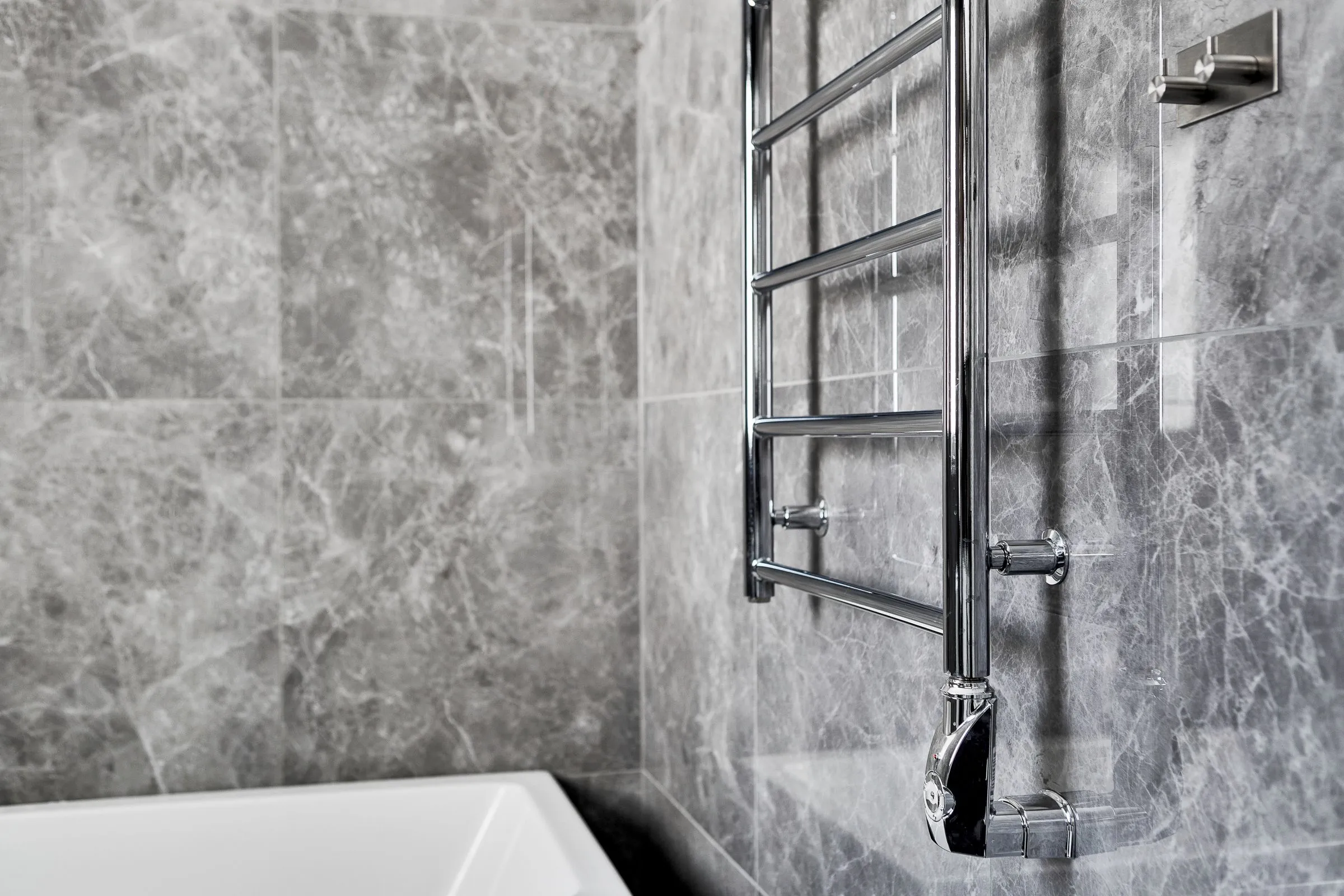 A bathroom with marble walls and a single slim steel towel rail.