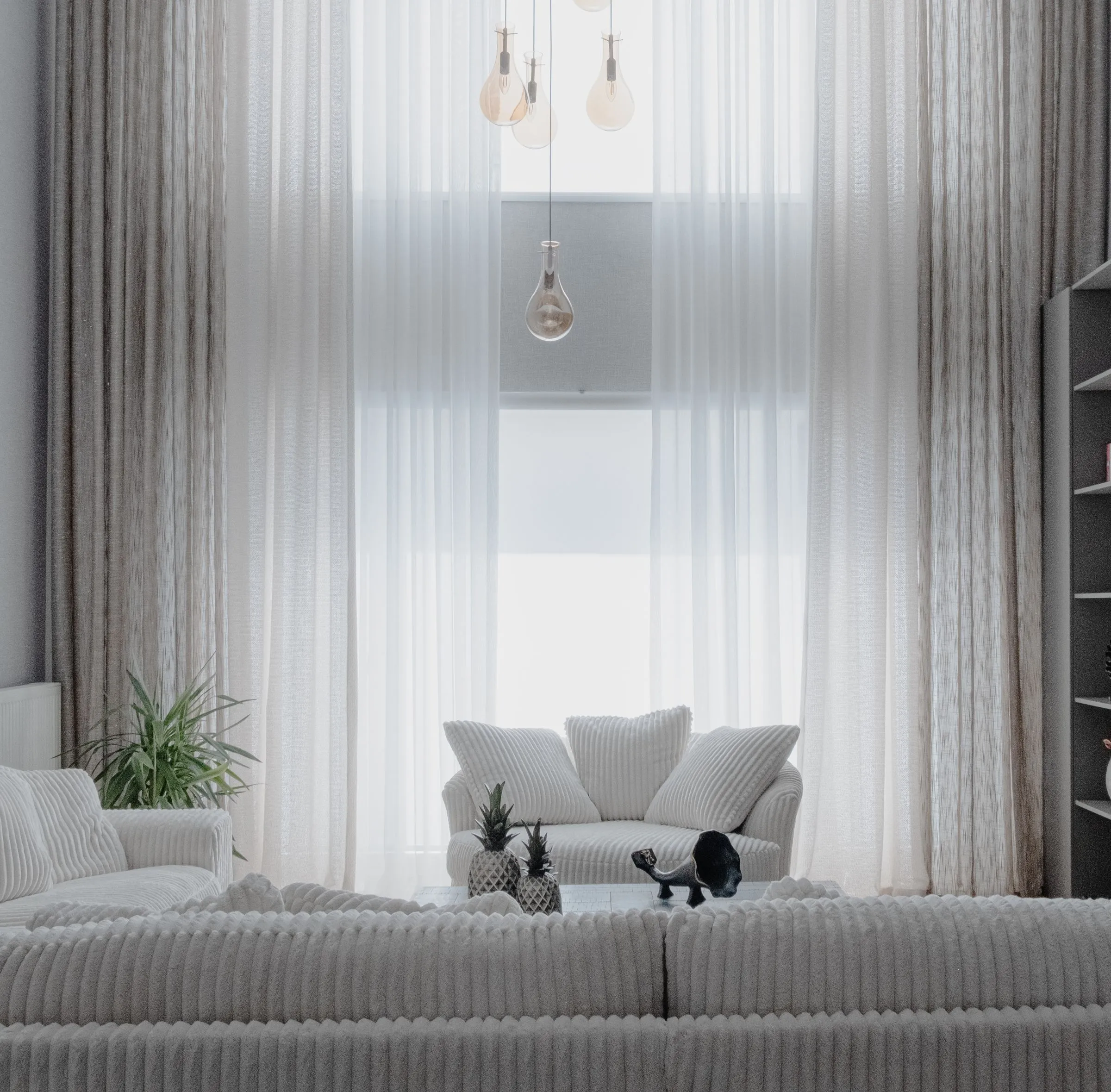 A pale living room with soft white sofas and long curtains at a tall window.