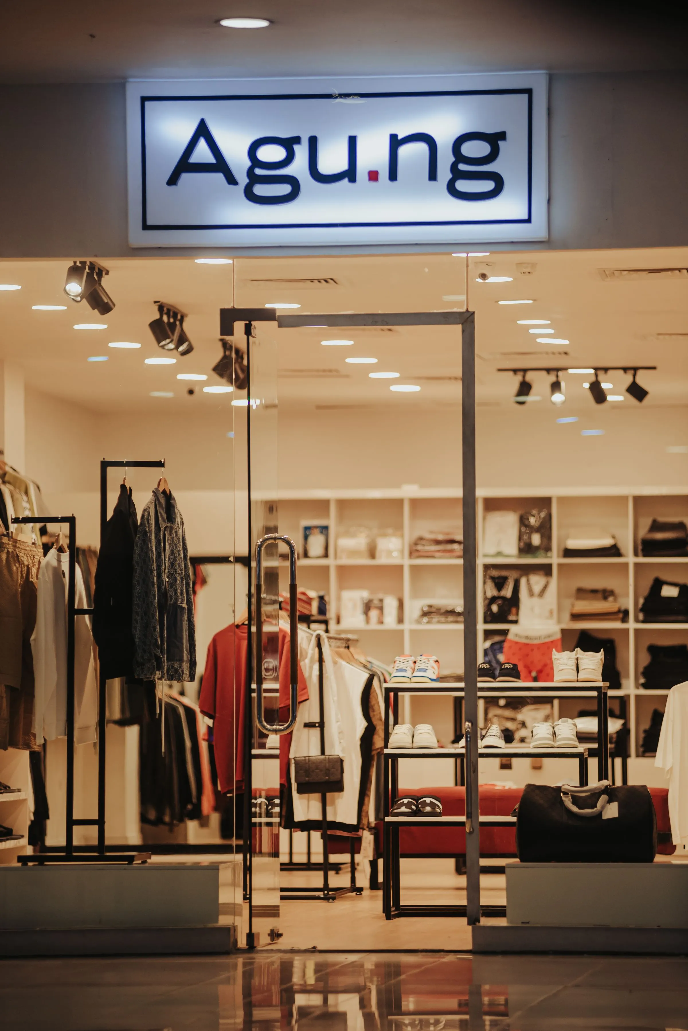 A clothing store with garments on rails and accessories under warm lighting.