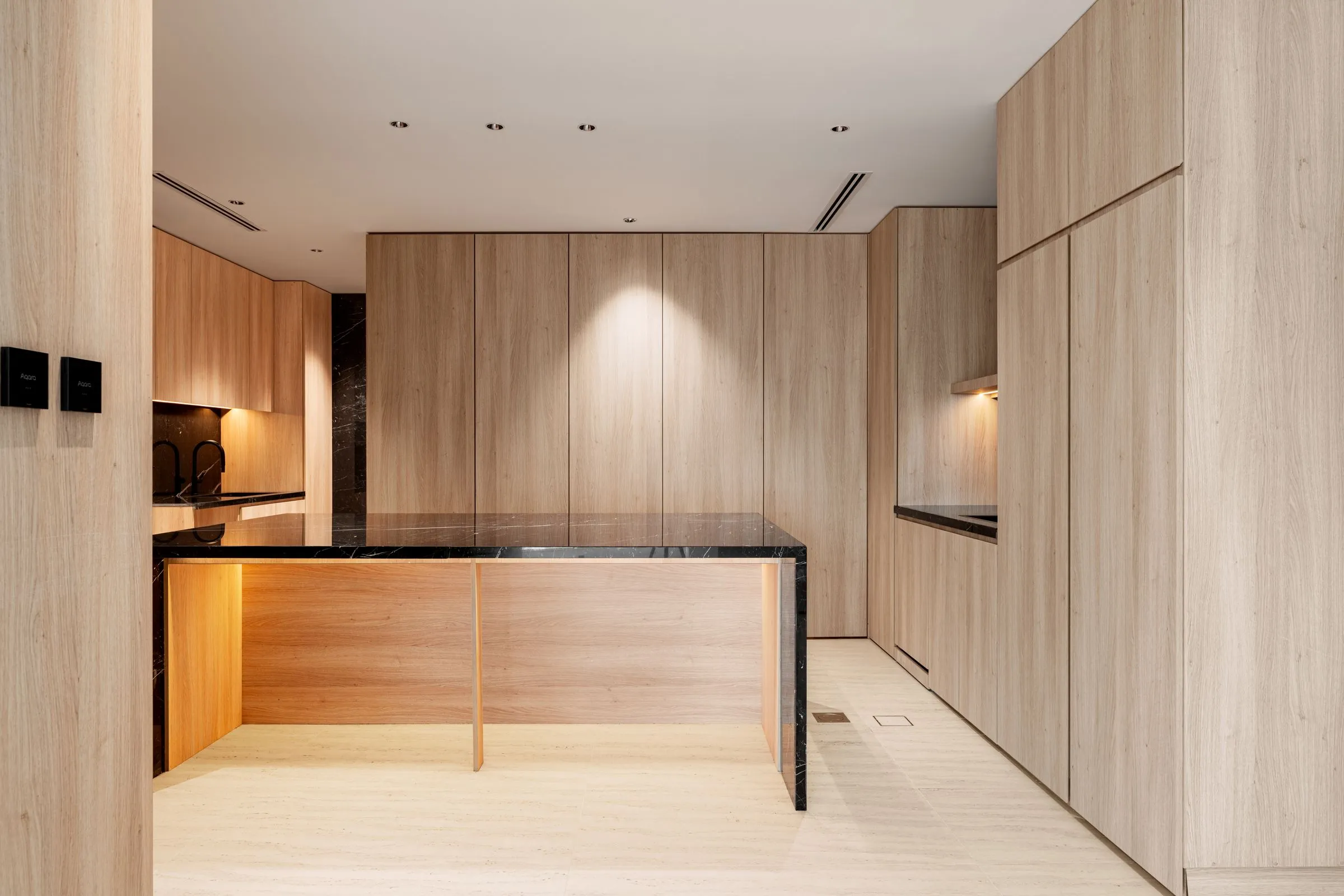 A kitchen with timber panelling, dark stone worktops and concealed lighting.