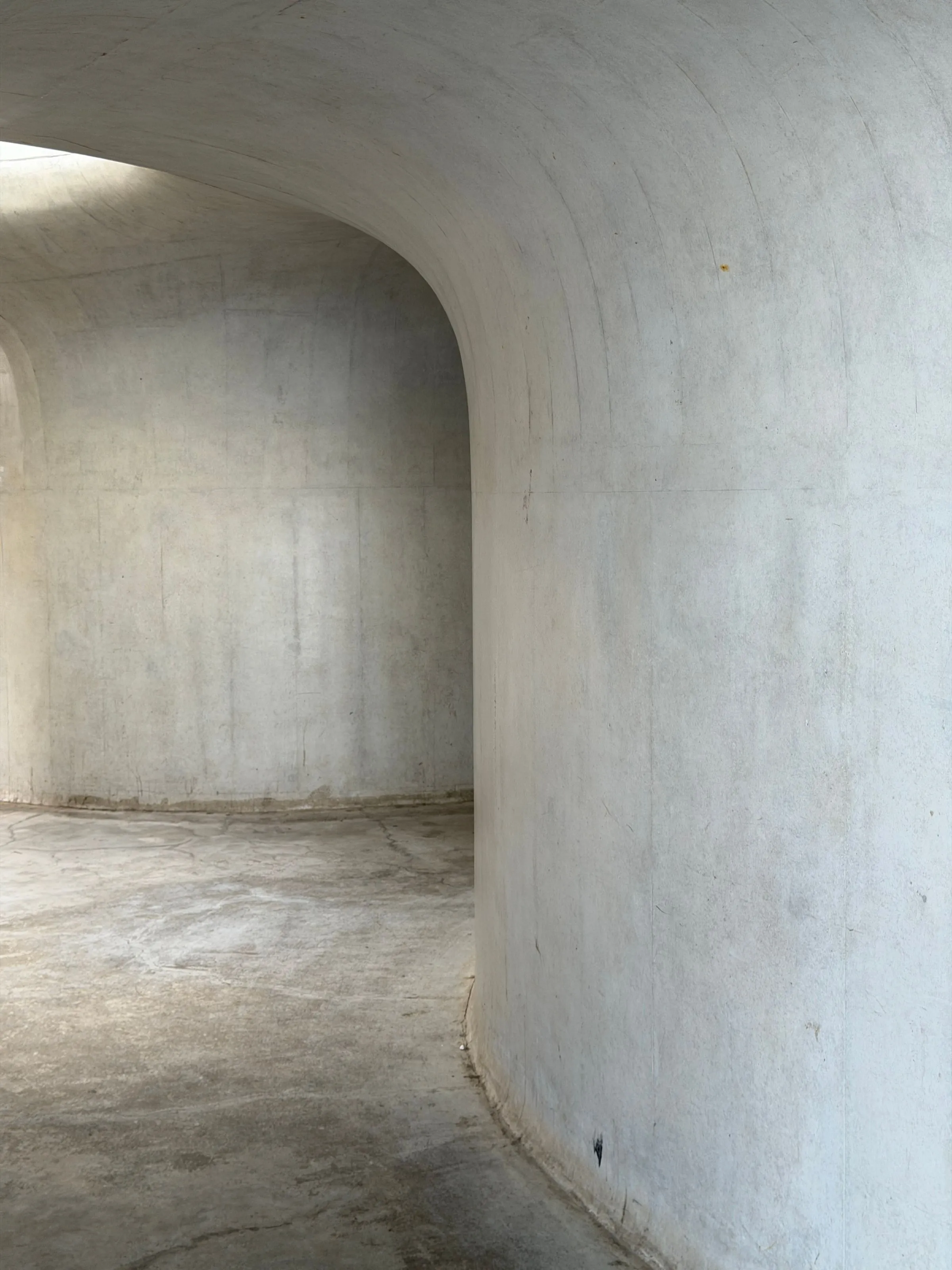 A long curved plaster wall meeting a bare floor, lit only from one side.