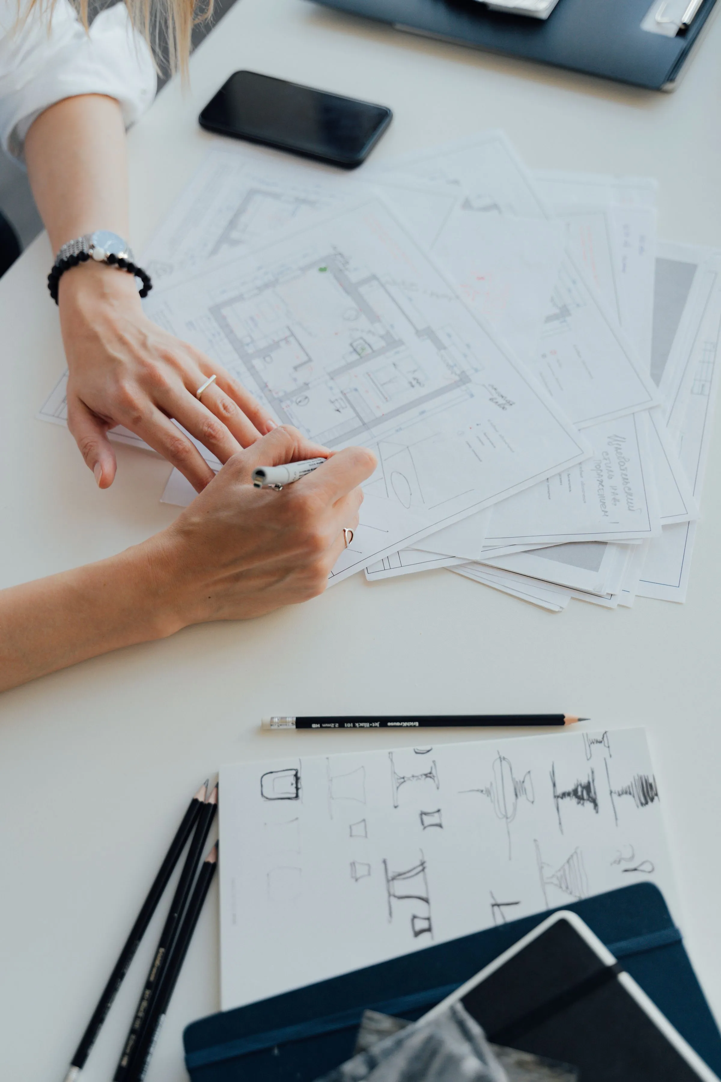 A designer's hands drafting a floor plan surrounded by drawing tools.