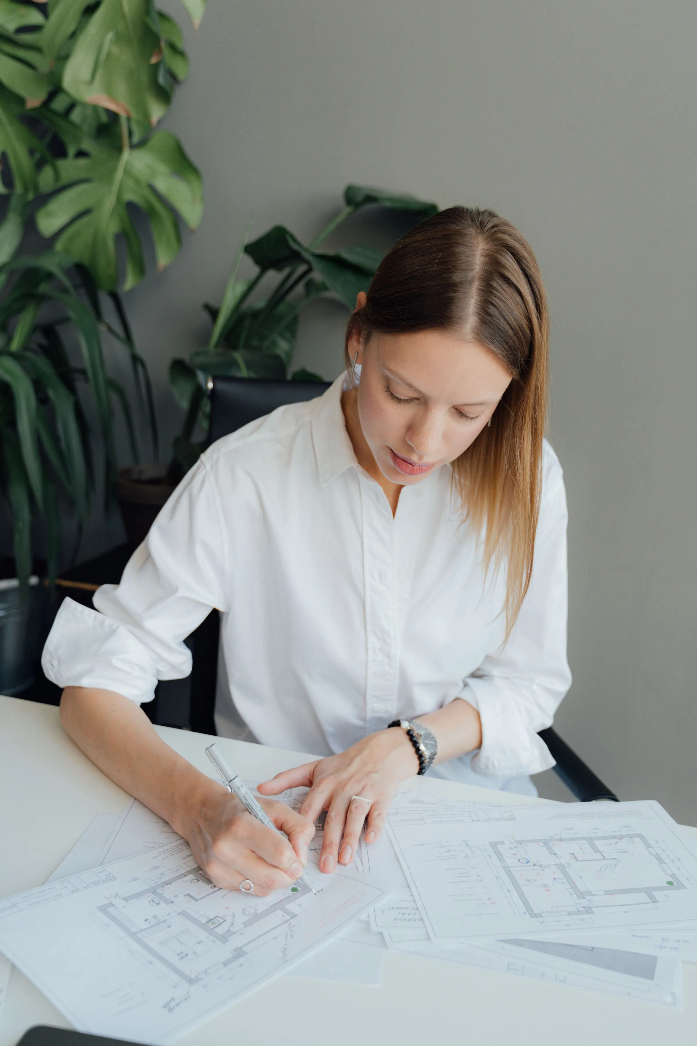 A designer checking floor plans at a desk surrounded by planting.