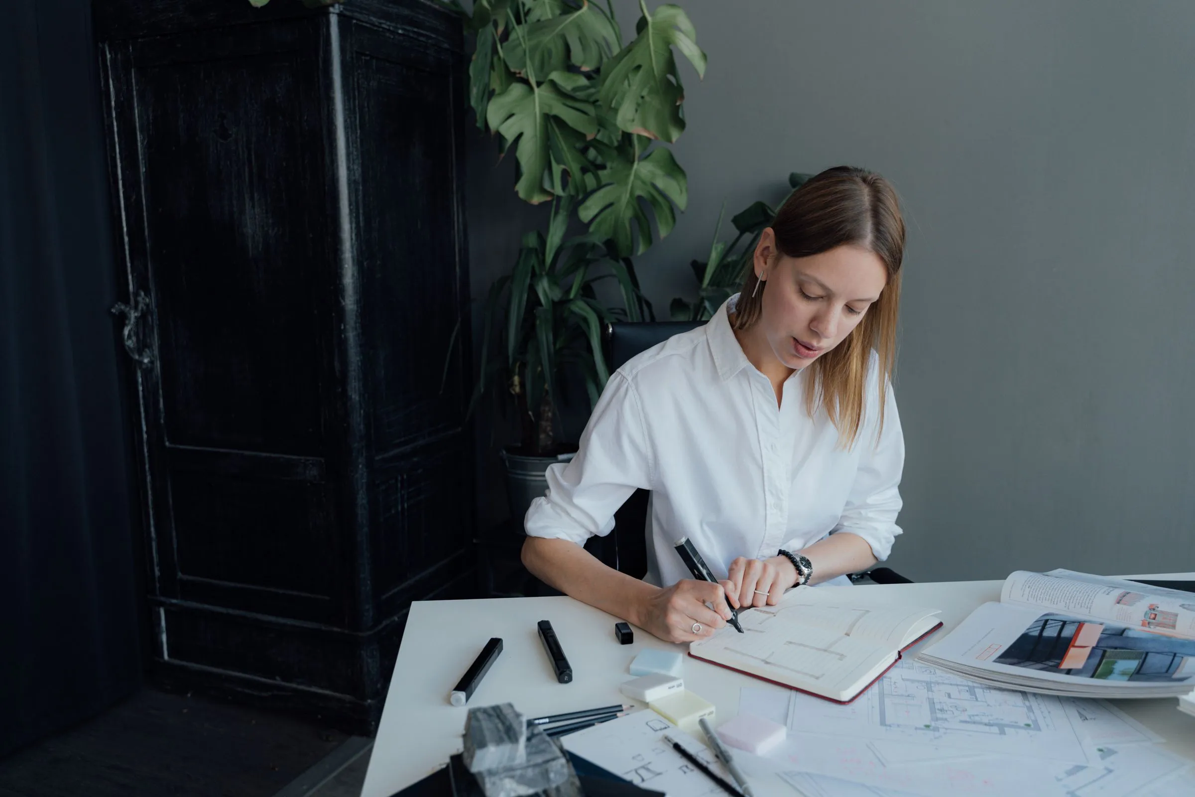 A designer working through floor plans at a desk beside a window.