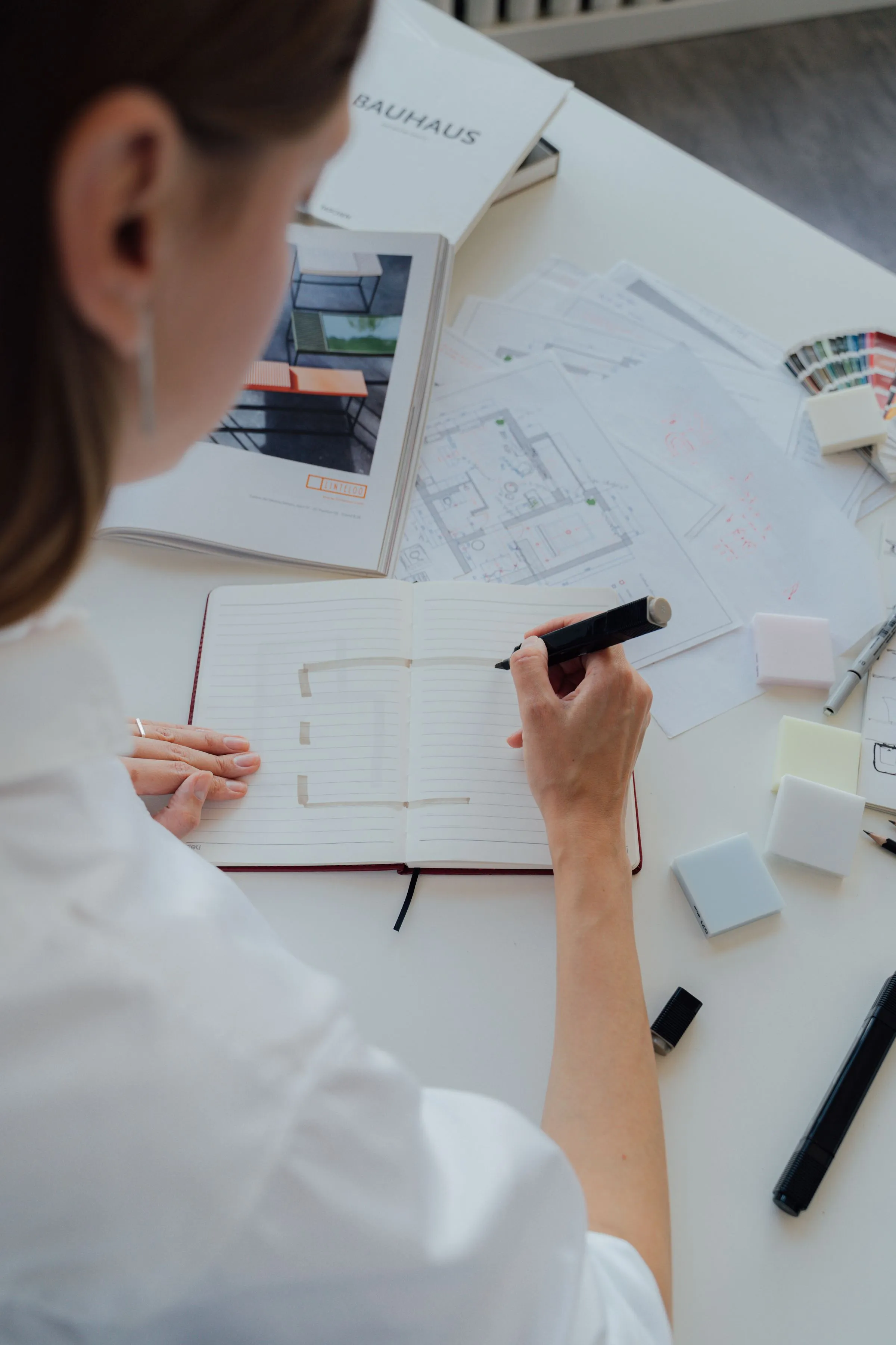 A designer sketching a floor plan with material samples spread across the desk.