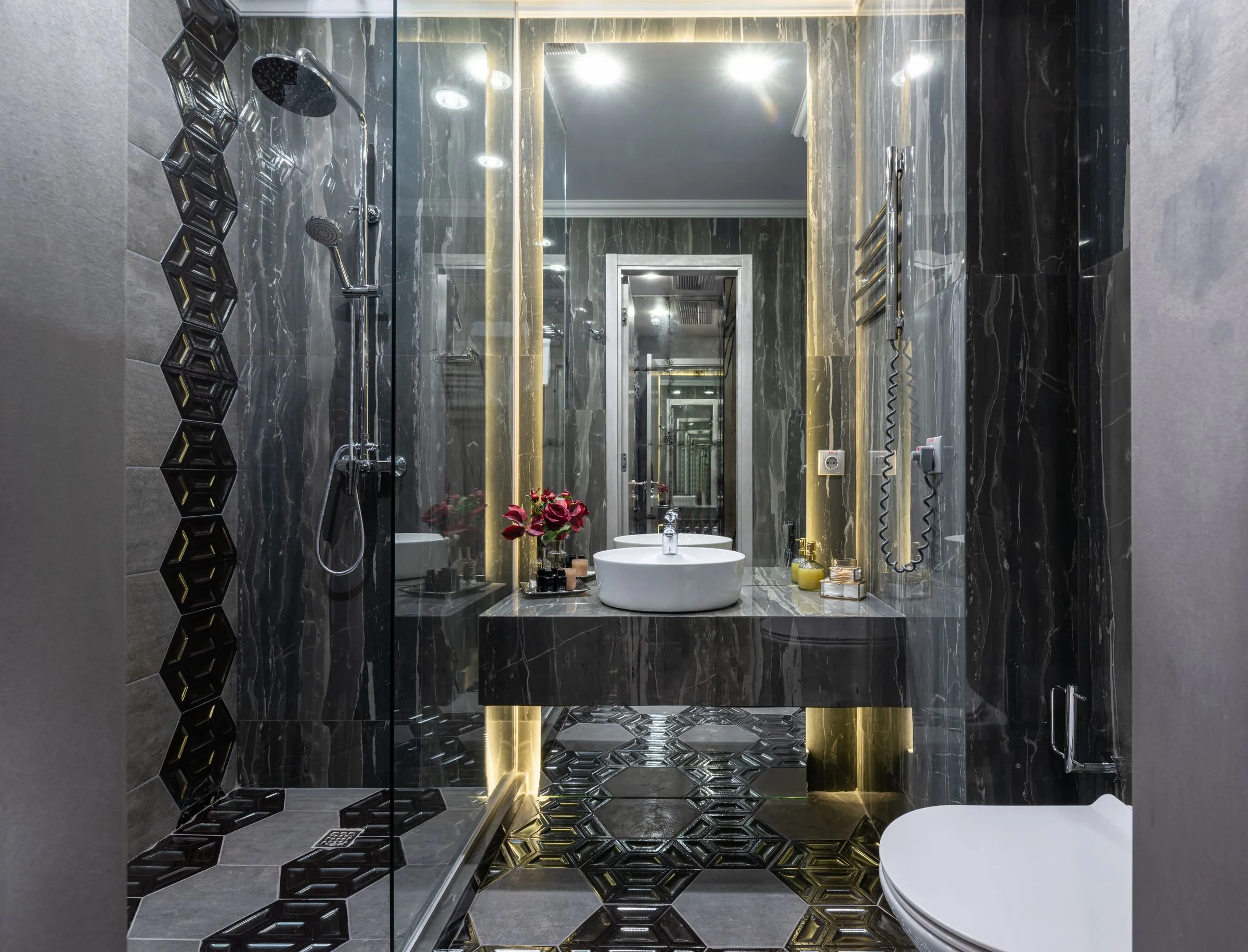 A bathroom with dark tiled walls and a glazed shower enclosure.