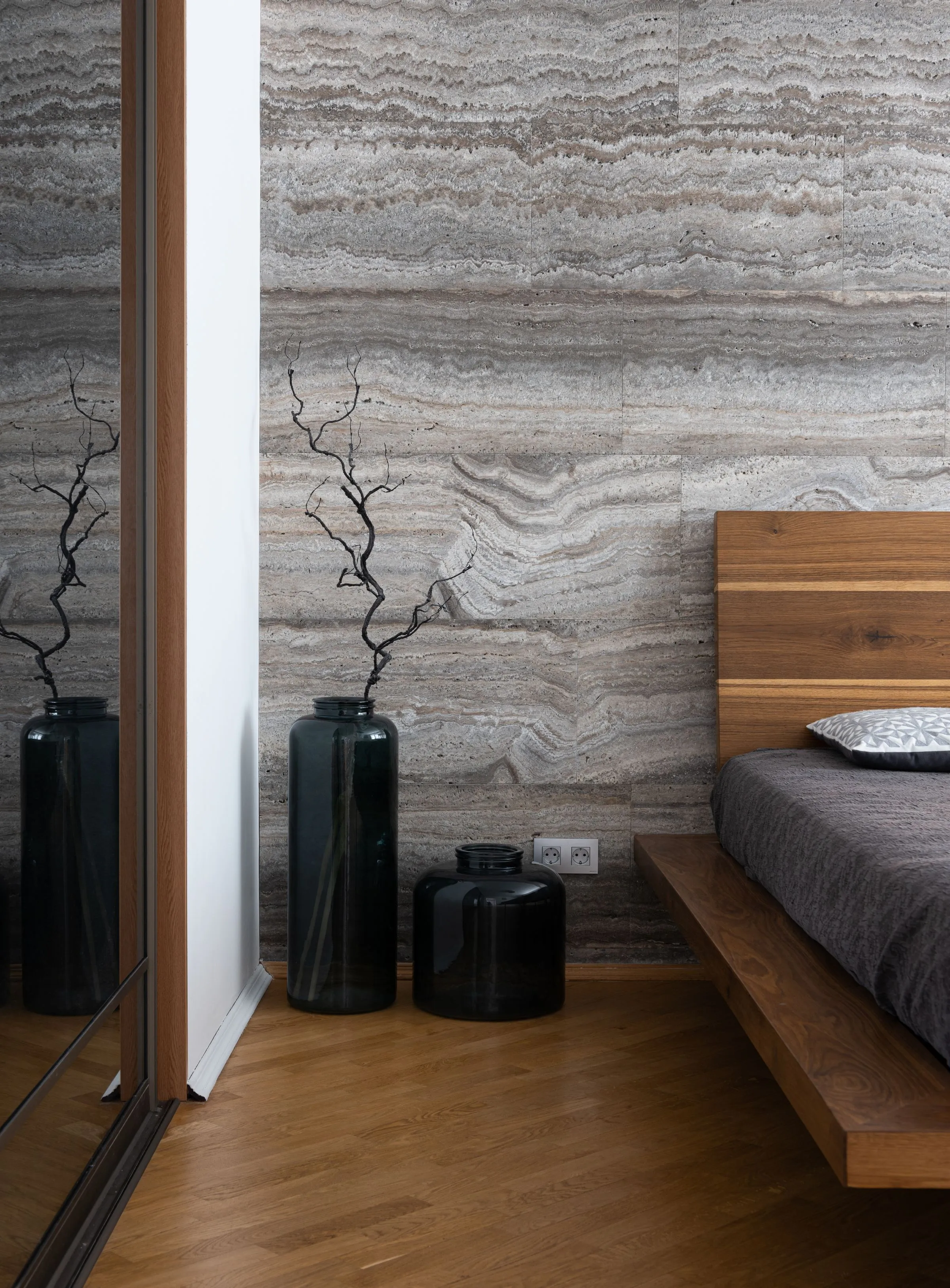 A small flat with a bed, a mirrored wall and branches in a tall vase.