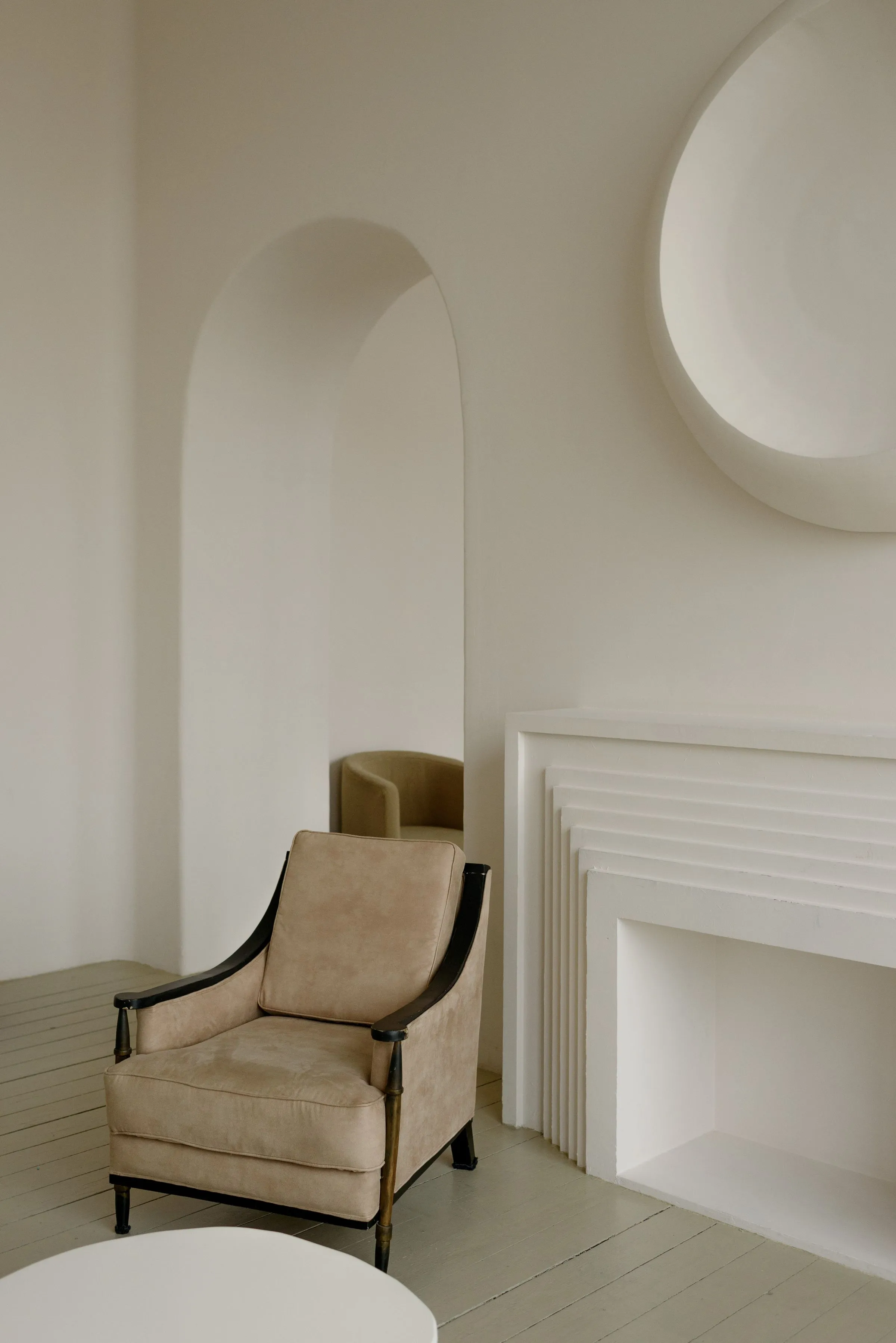 A beige armchair standing beside an arched plaster niche and a plain fireplace.