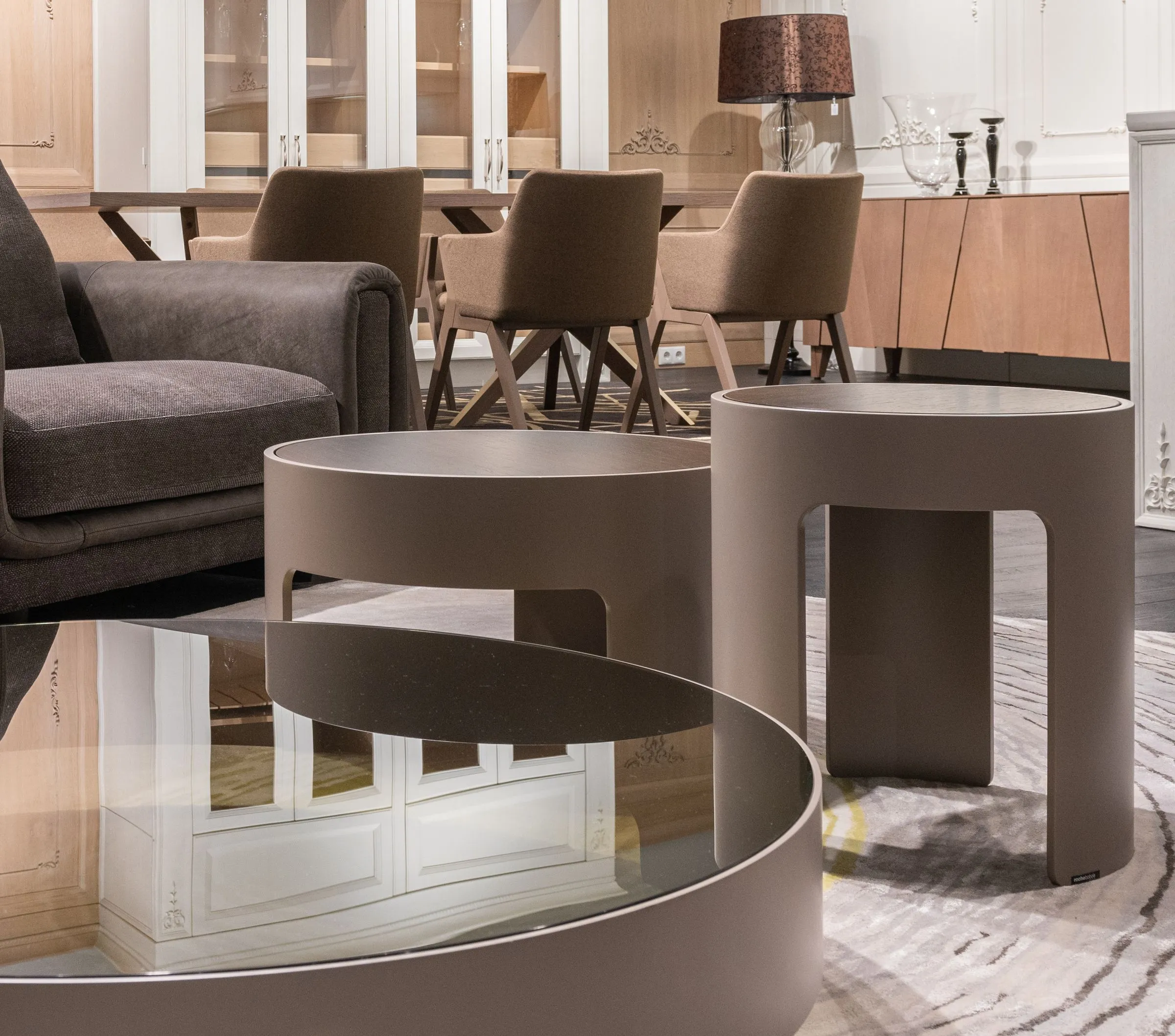 Two small round tables beside a sofa, with a lamp on a timber cupboard behind.