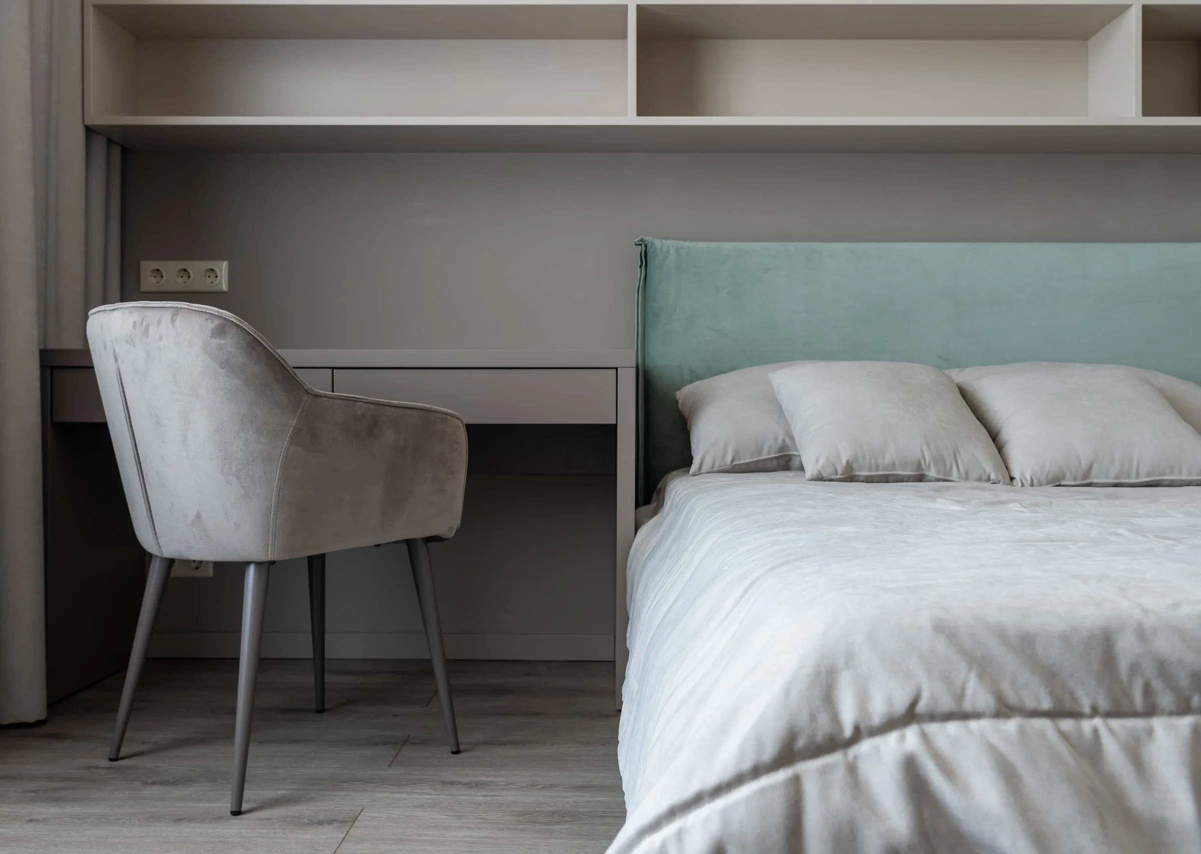 A light bedroom with a made bed, a small table and open shelving above.