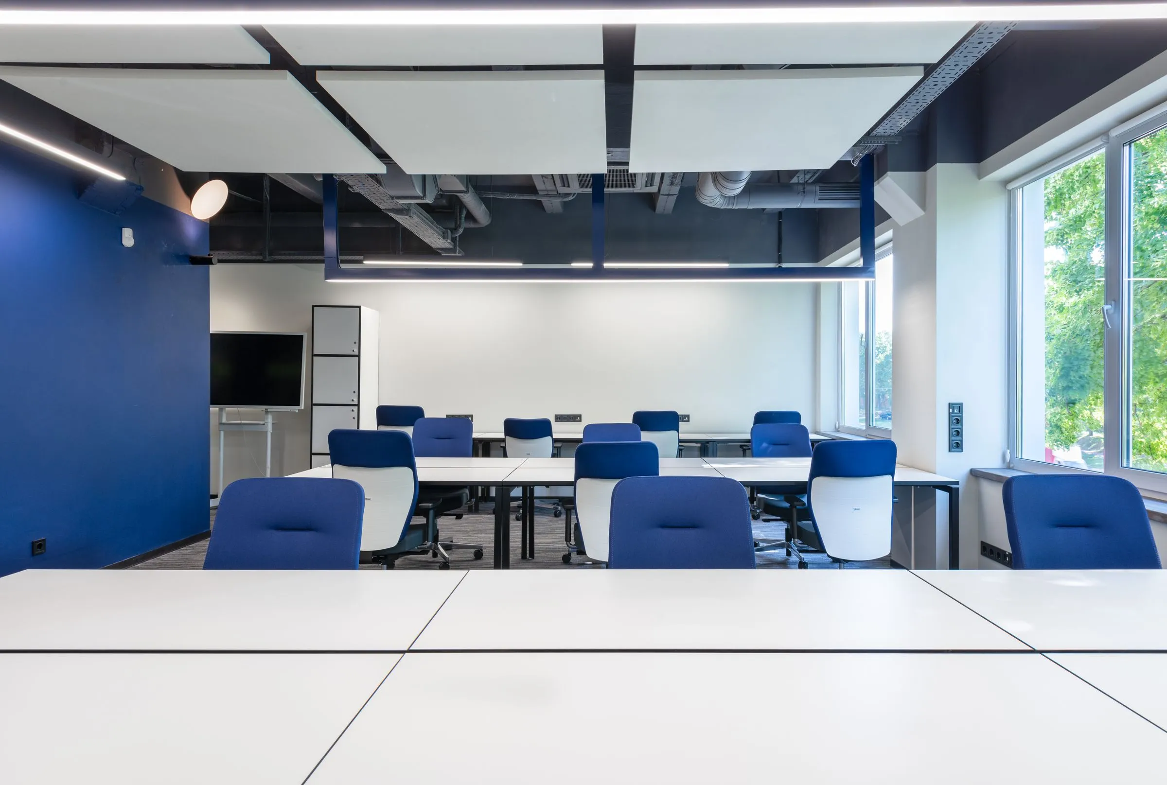 Rows of workstations at Atelier 27 beside a full-height window overlooking the city.