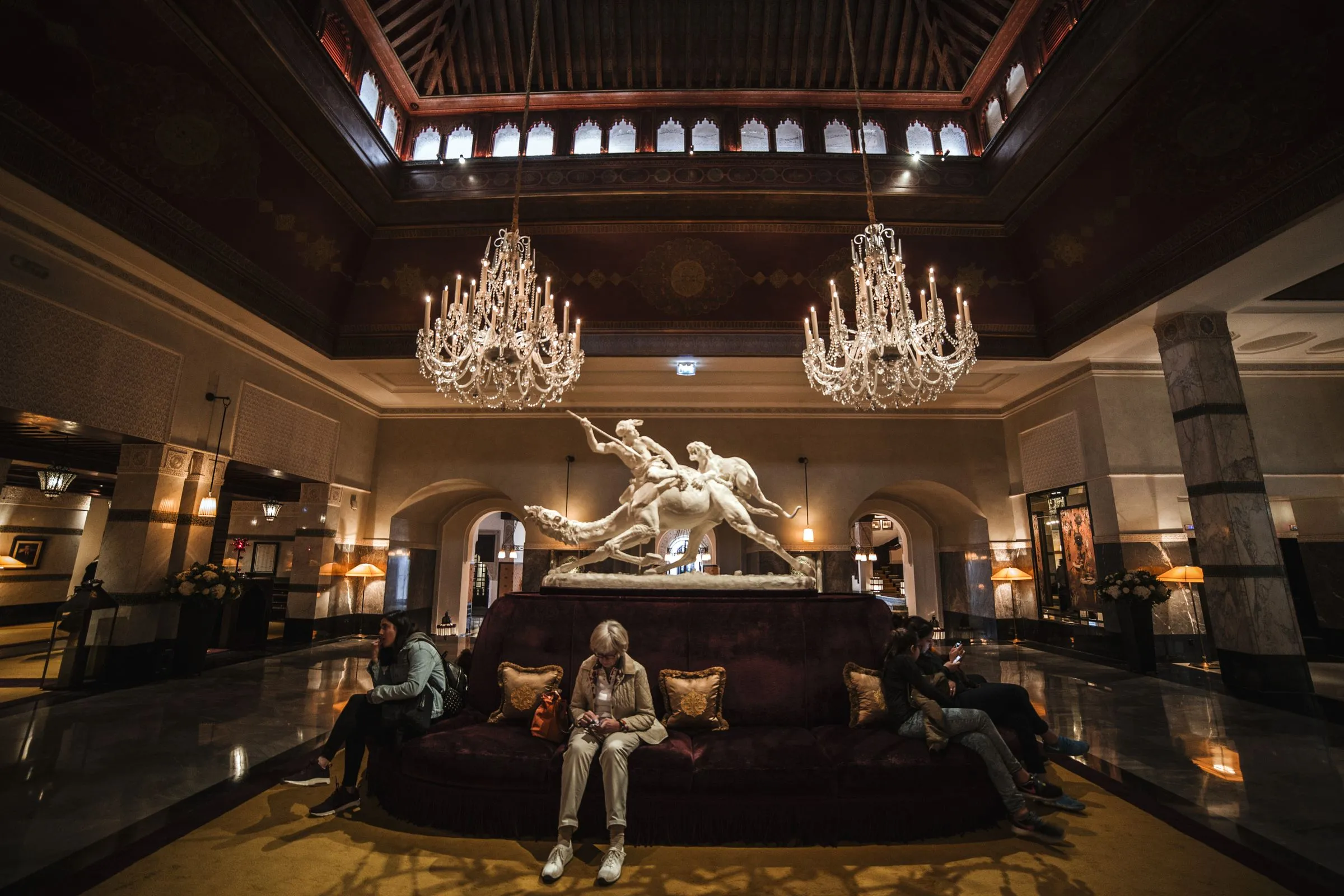 Guests seated in the double-height hall at Hotel Marana beneath a crystal chandelier.
