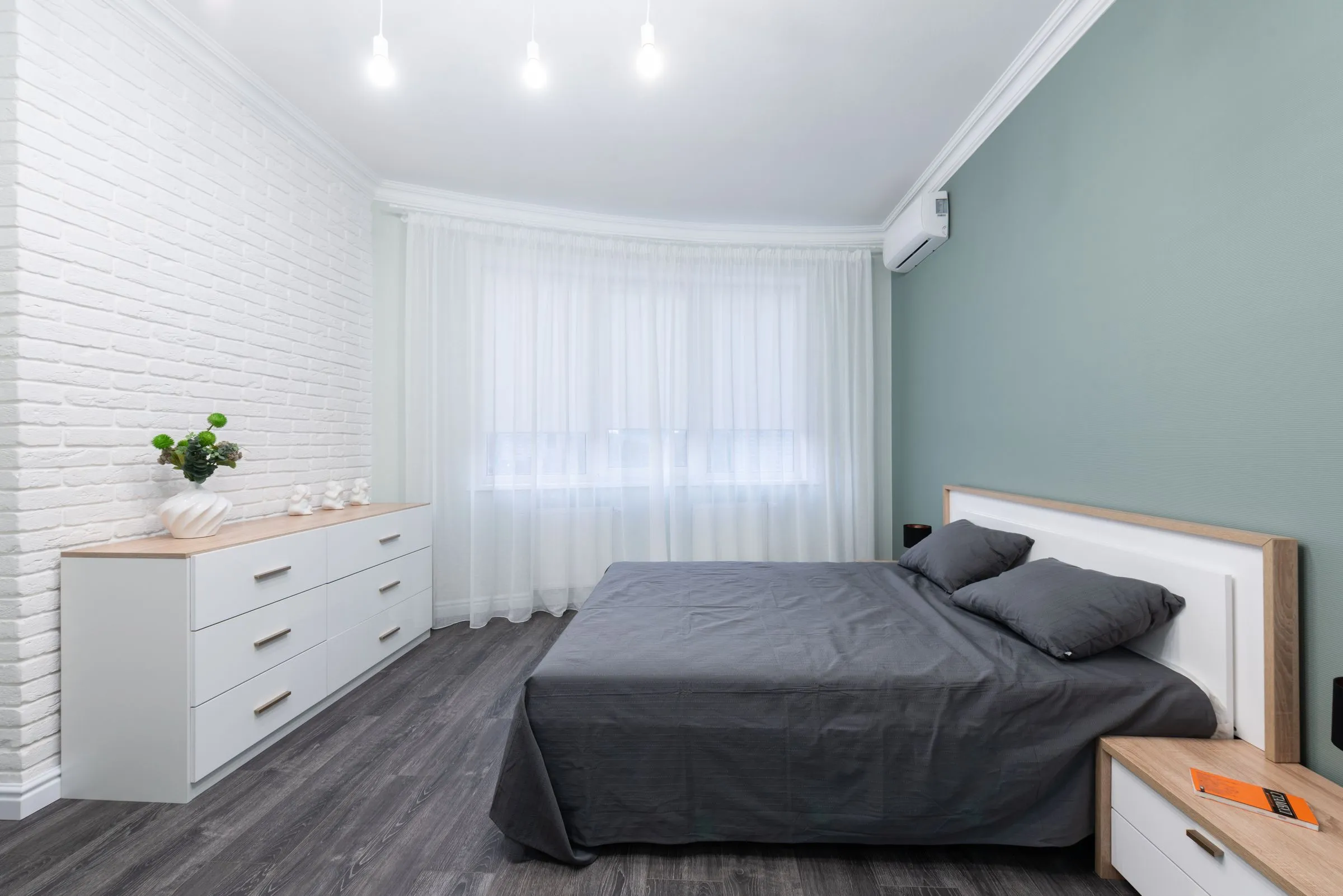 A bedroom lit by a row of exposed warm bulbs above a chest of drawers.