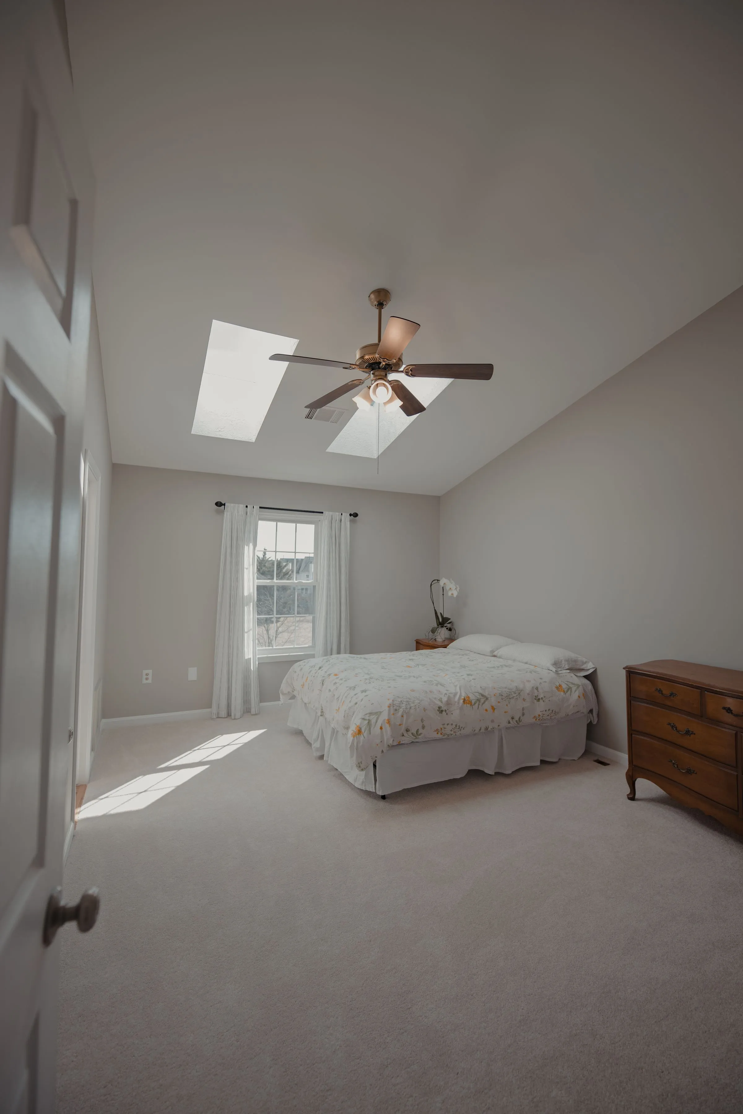 A compact bedroom lit by skylights, with a low bed and pale walls.