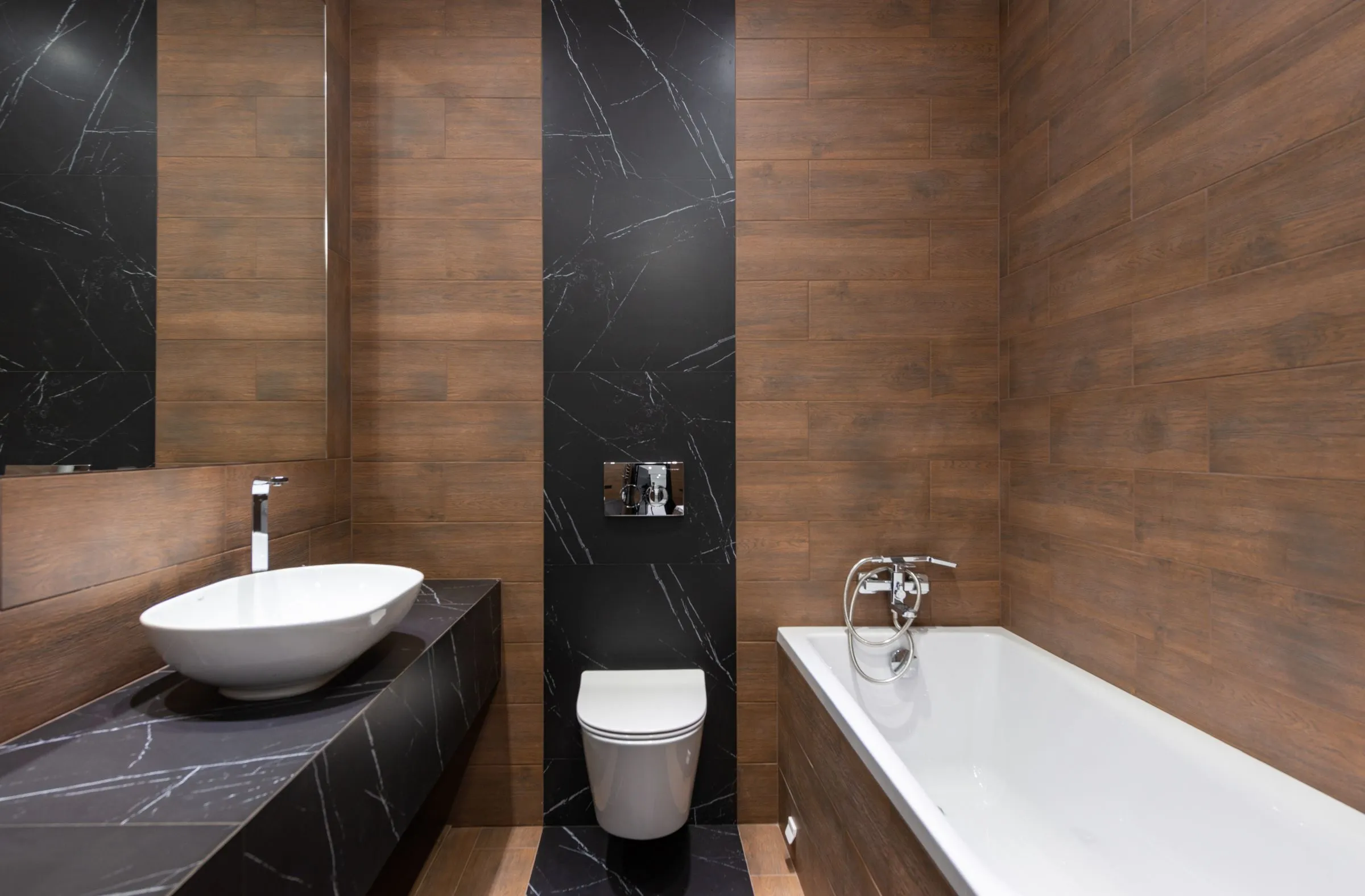 Bathroom at The Oak House lined with timber panelling and pale marble around a white basin.
