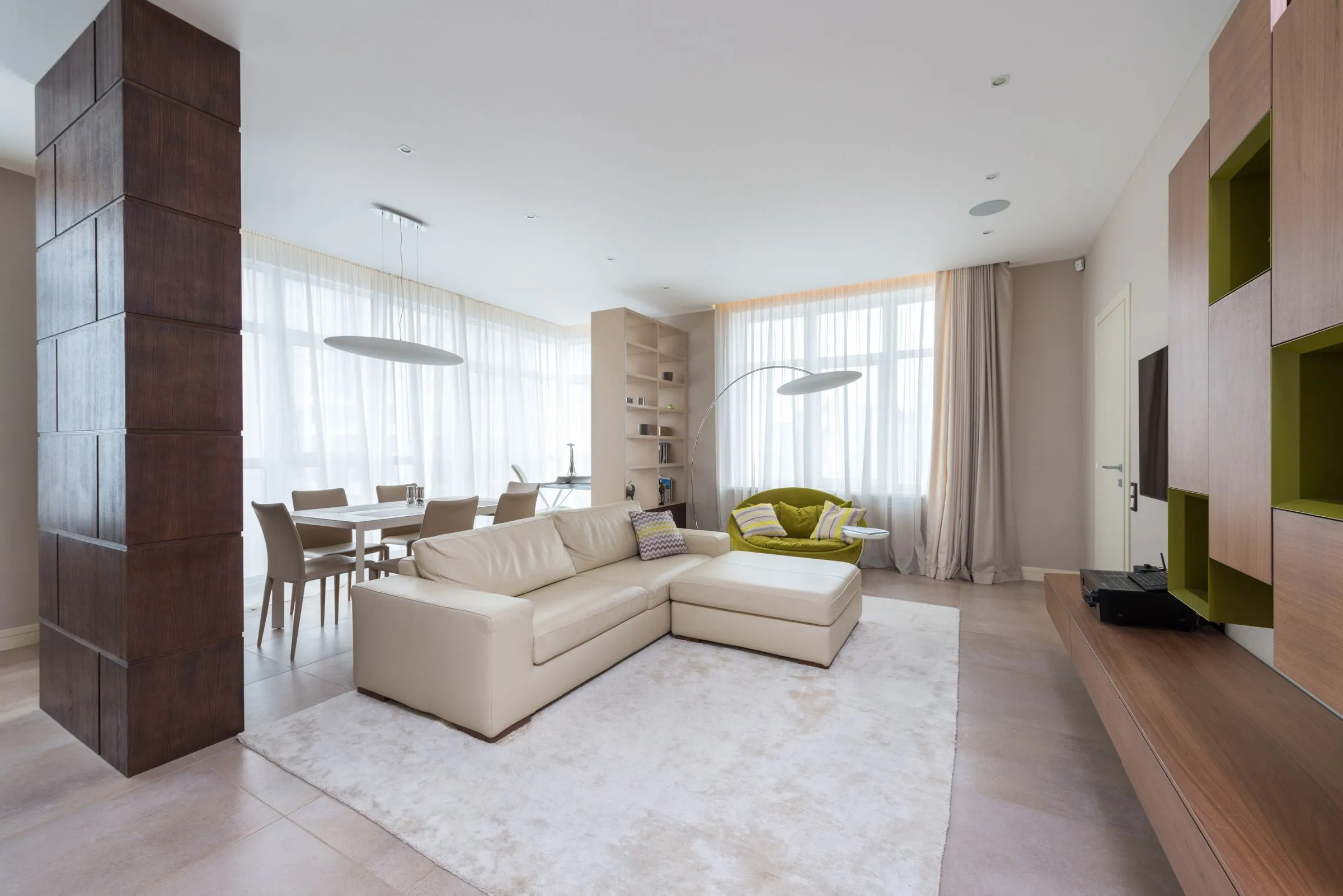 A spacious living room with a long sofa and daylight from a full-height window.