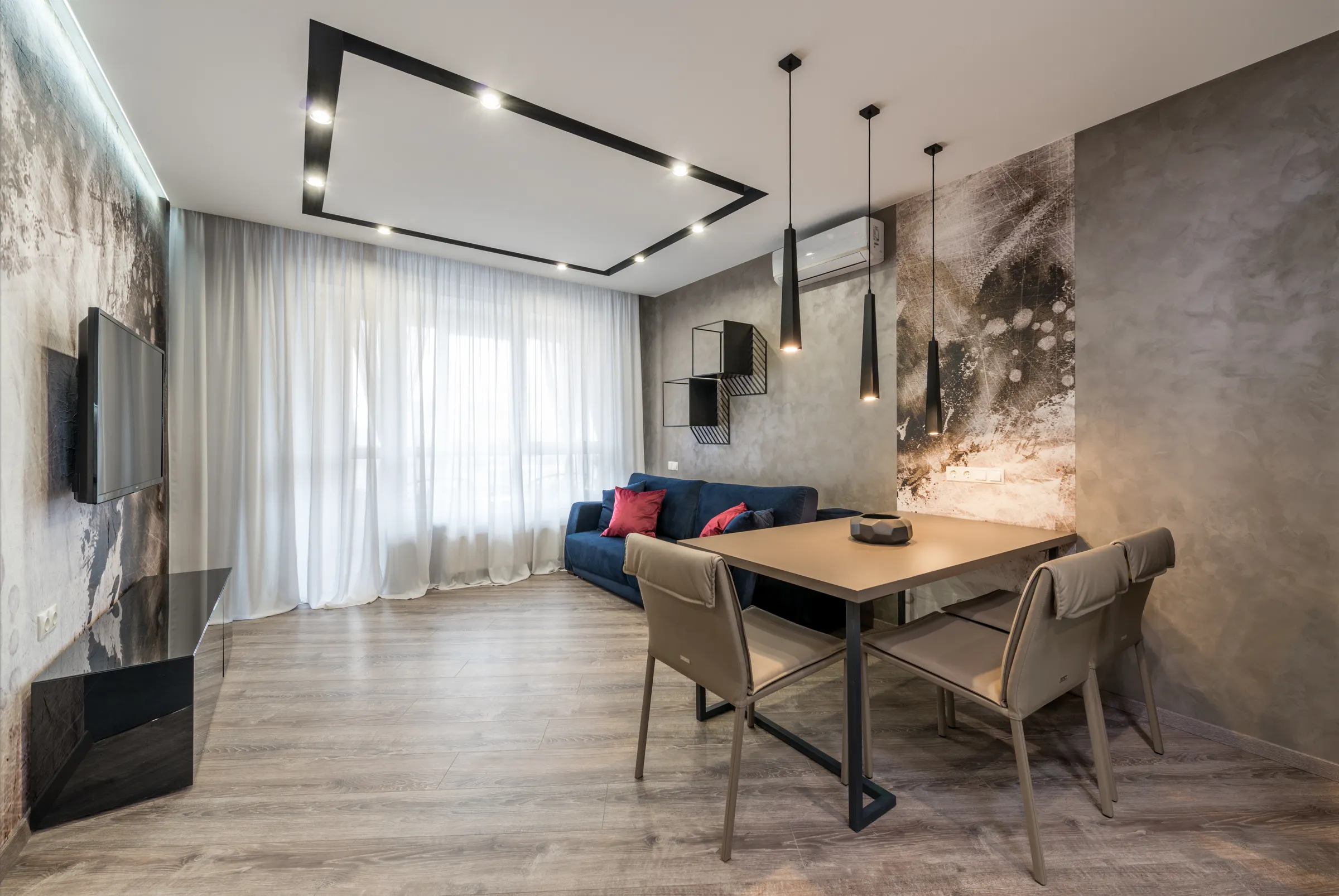 A timber dining table and chairs against a plain grey wall in a quiet living space.