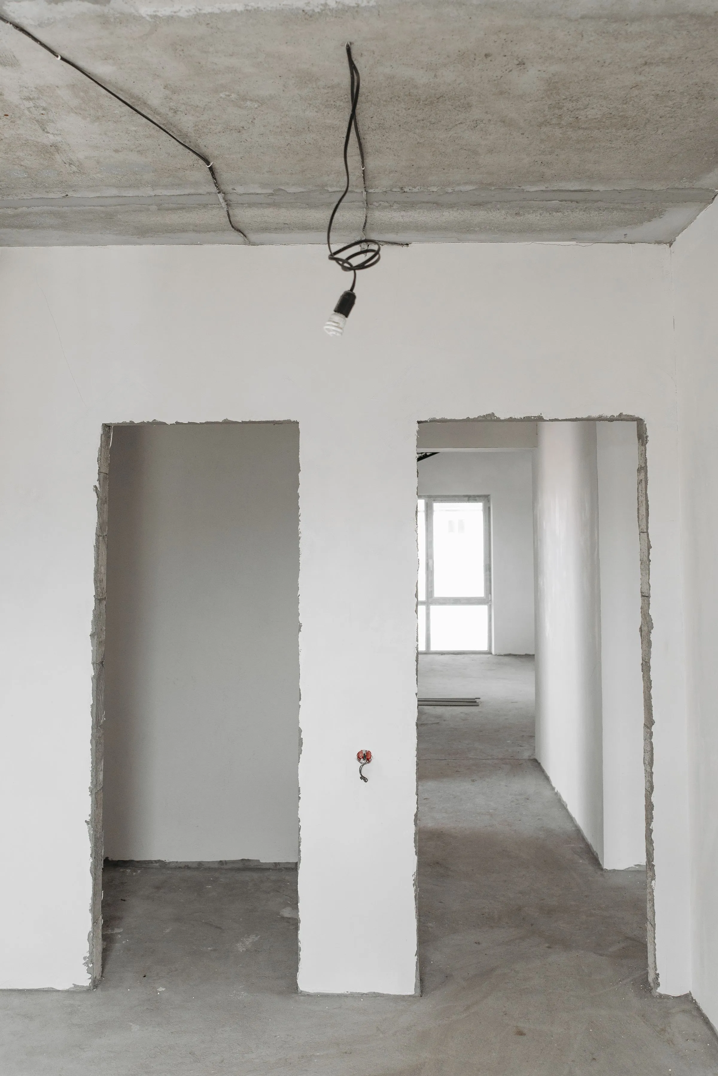 An unfinished room with bare plastered walls, an exposed ceiling and new door openings.