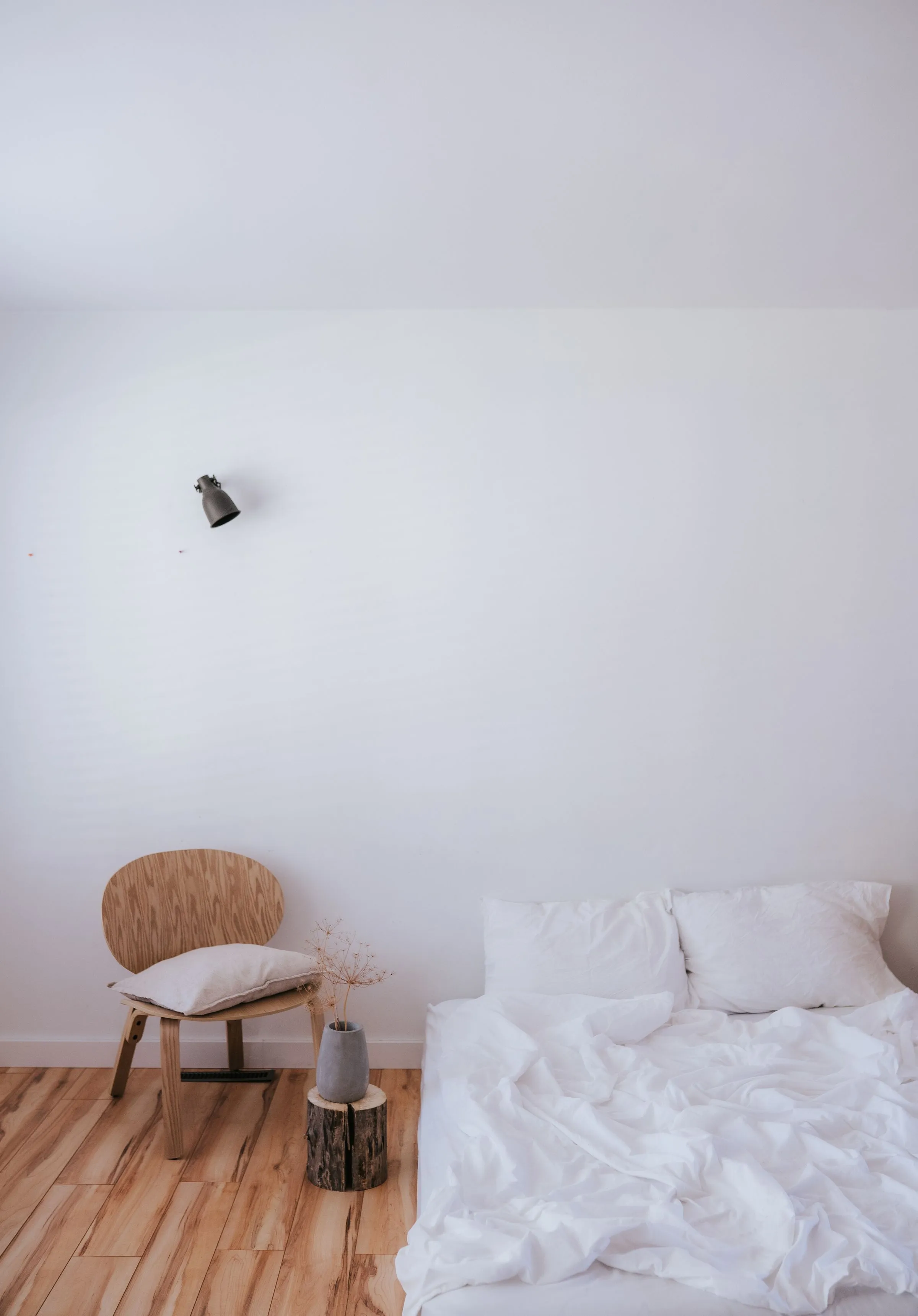 A Scandinavian-style bedroom with a white bed and a single timber chair.