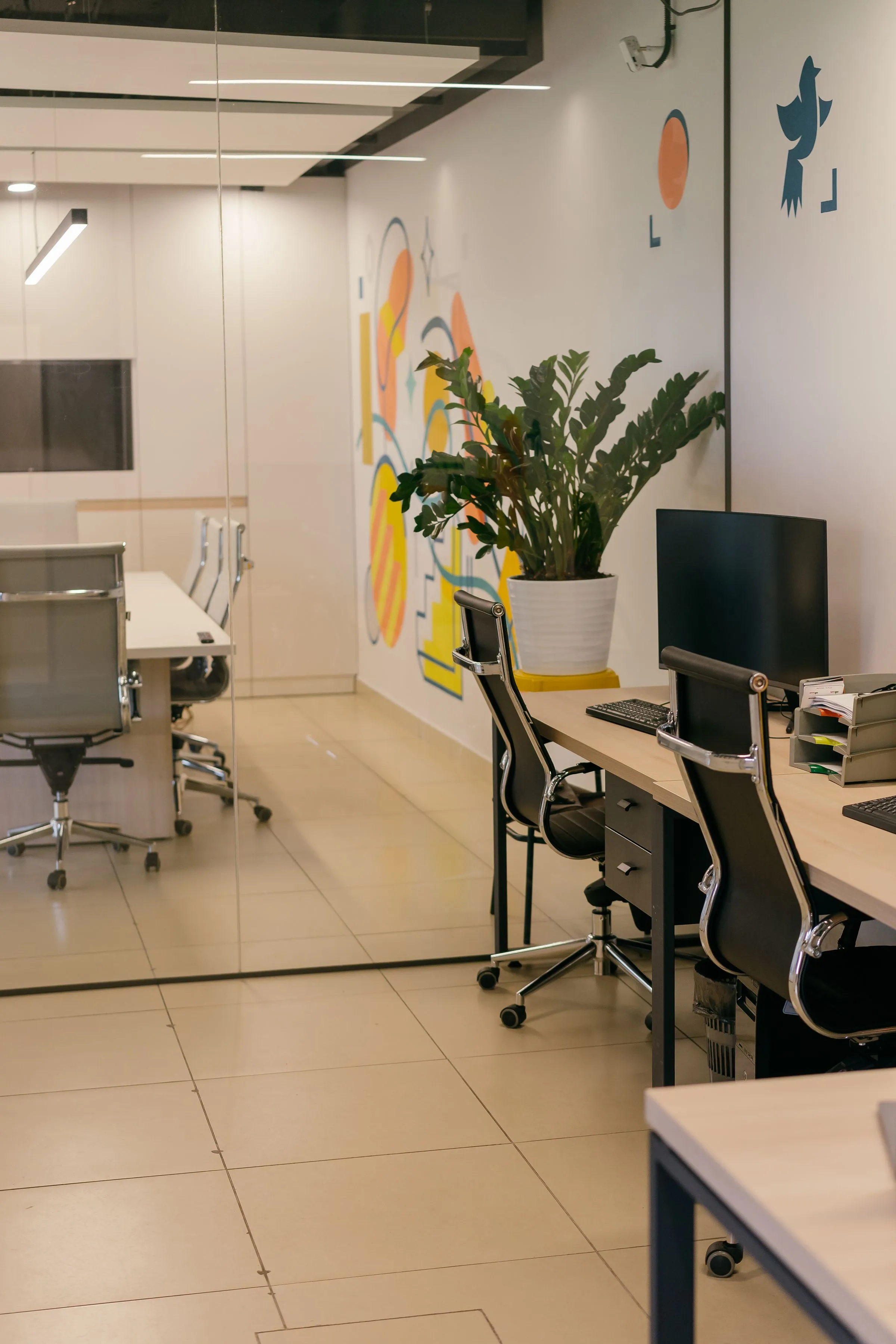 A contemporary office with glass partitions, planting and open workstations.