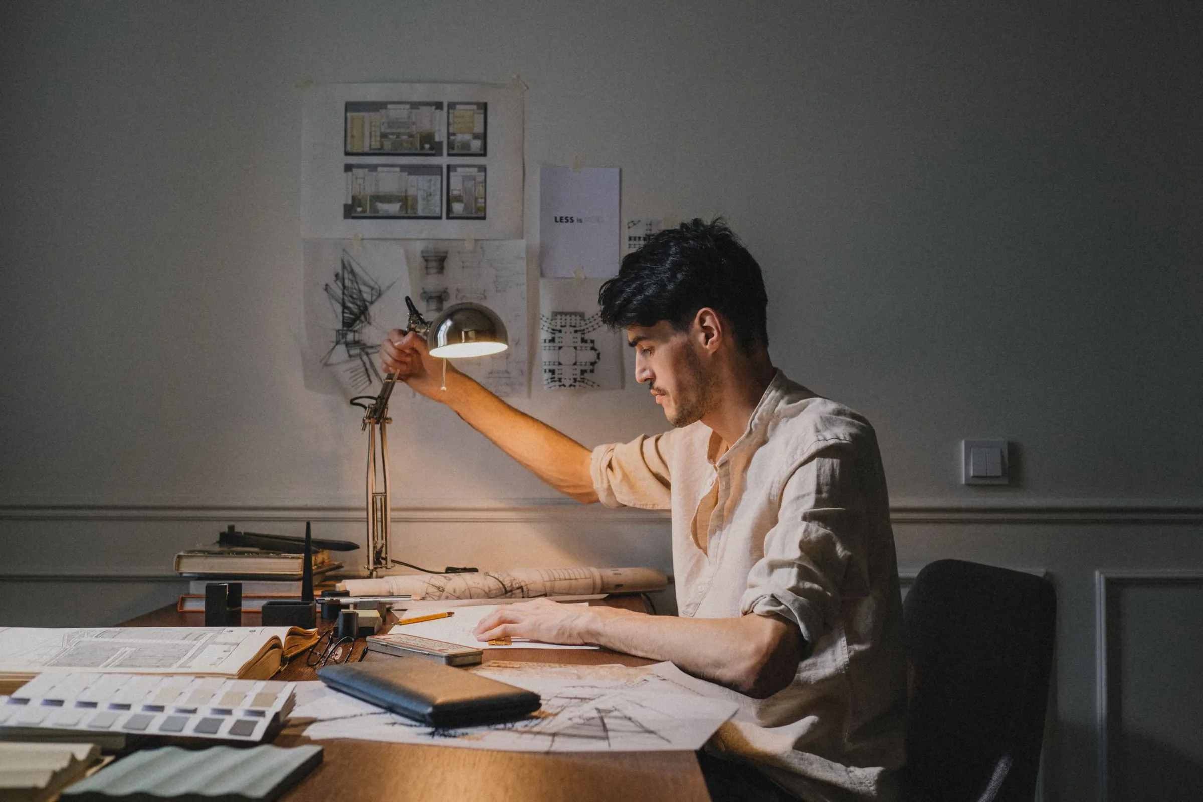 An architect working over drawings at a desk under a single task light.