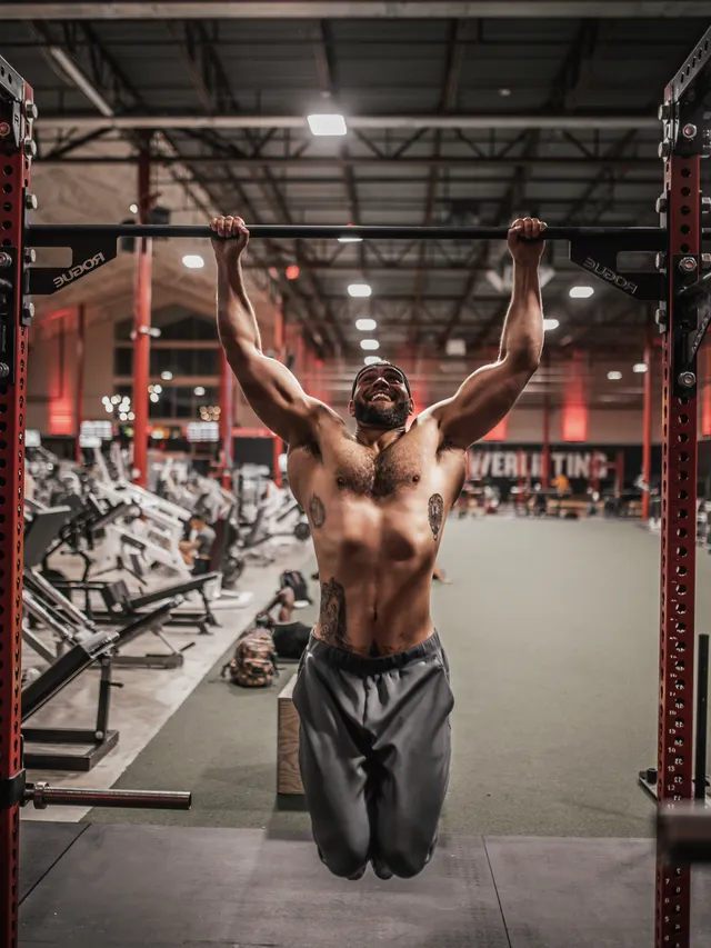 Athlete mid pull-up on a rig in an industrial training hall