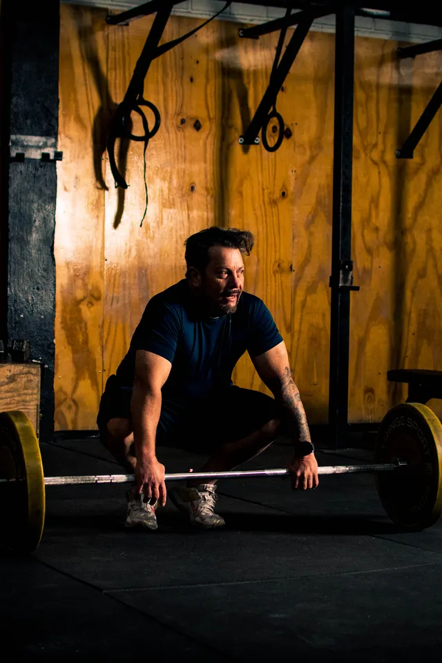Lifter setting up under a loaded barbell in a dimly lit training hall