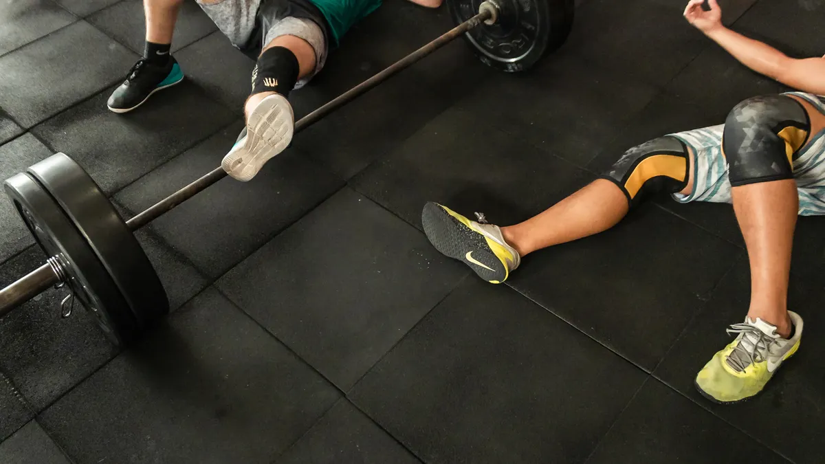 Two athletes recovering on the floor beside loaded barbells