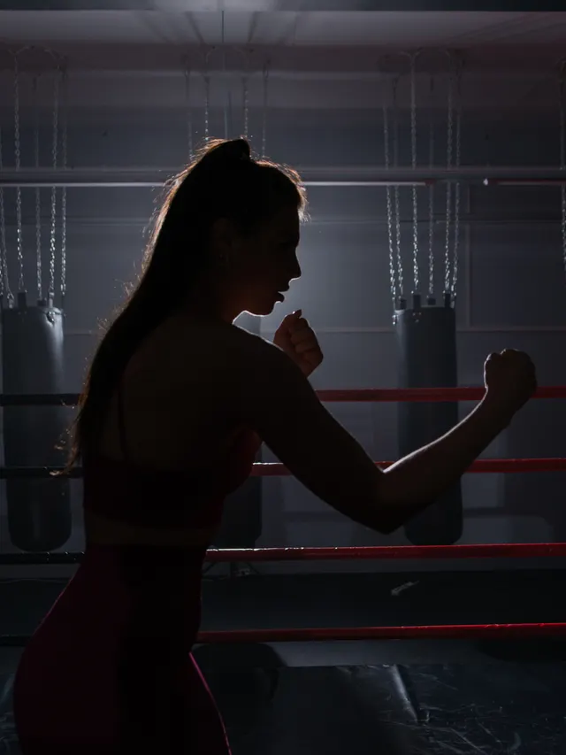 Boxer working the bag, lit from behind in a dark room