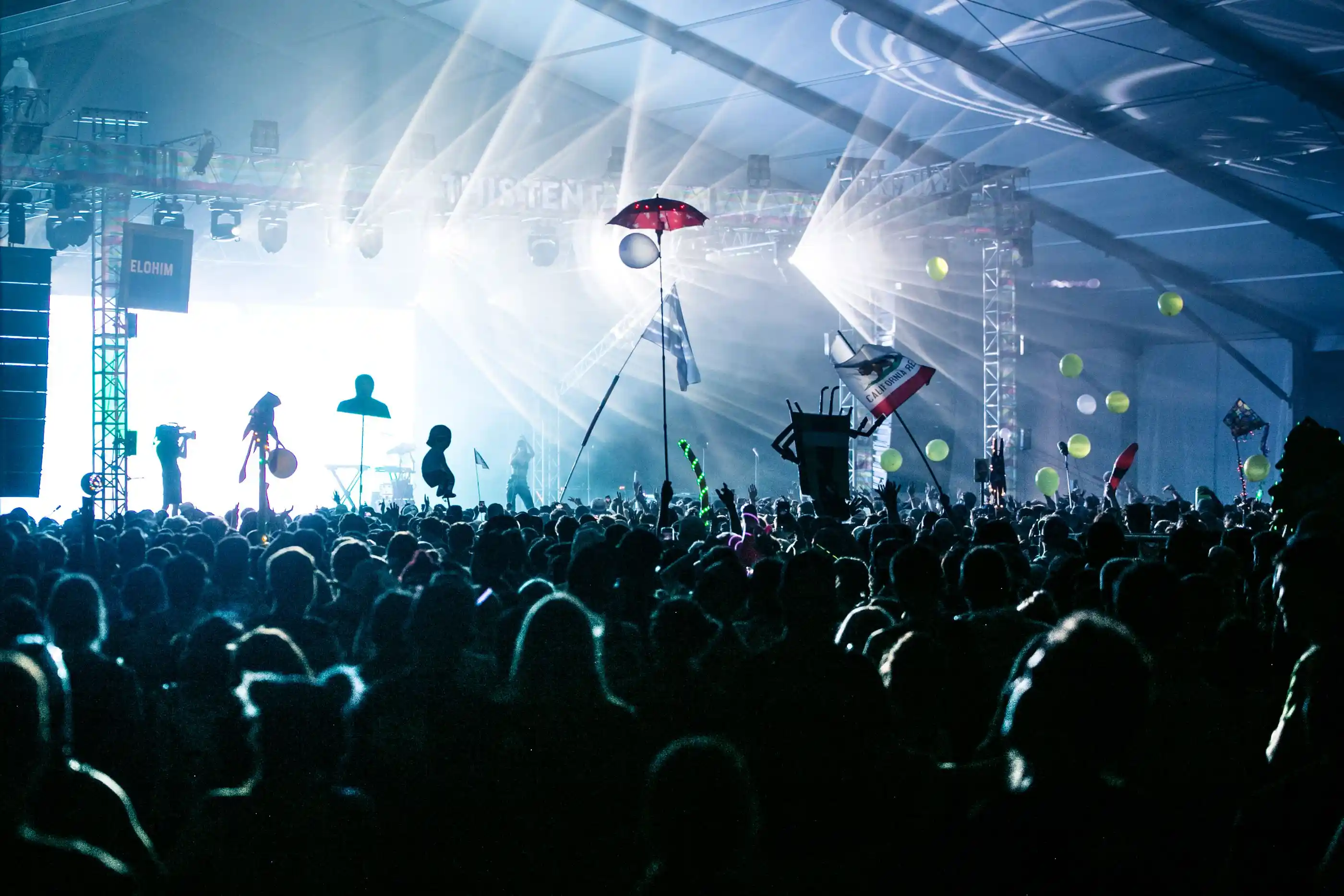 A concert crowd with arms raised beneath white beam lighting
