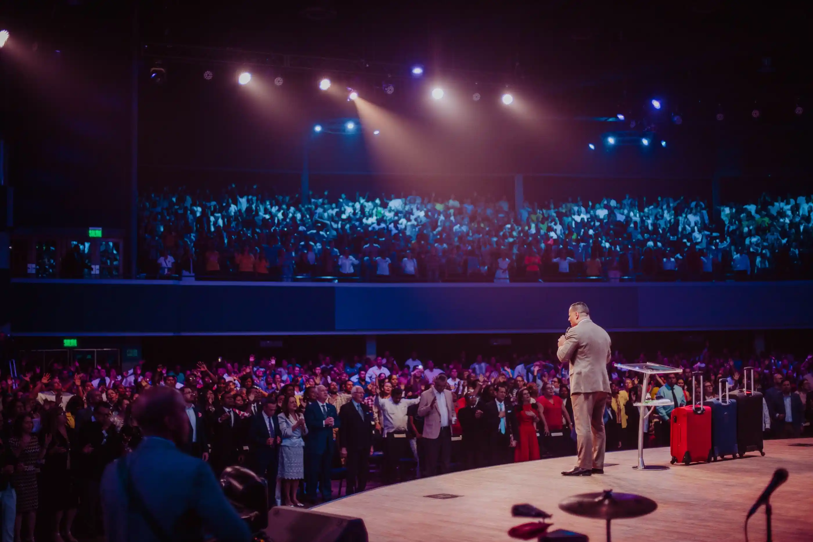 A speaker on a lit stage addressing a full auditorium from behind a lectern