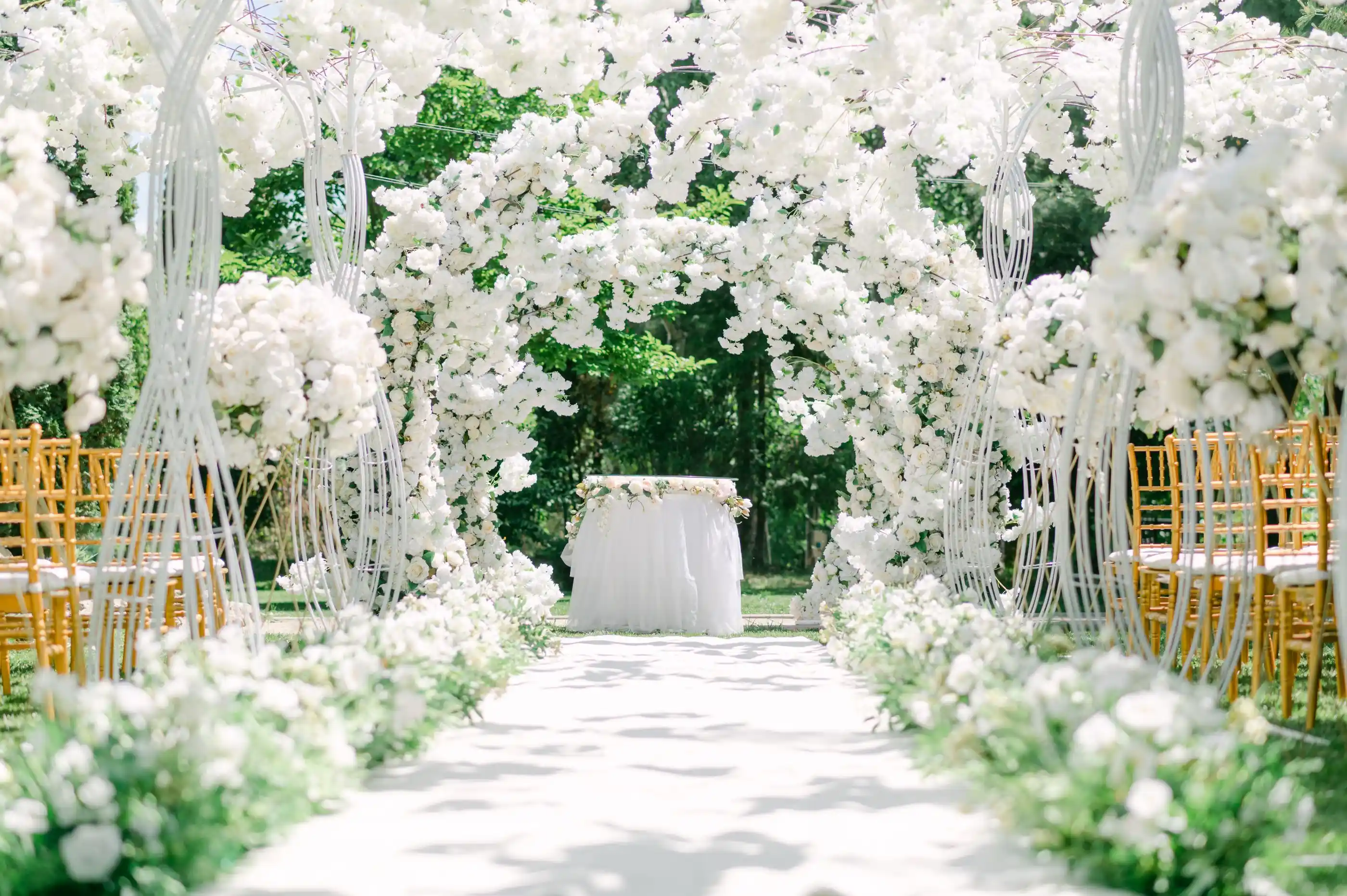 A white floral arch over an aisle laid across pale stone, chairs set in rows either side