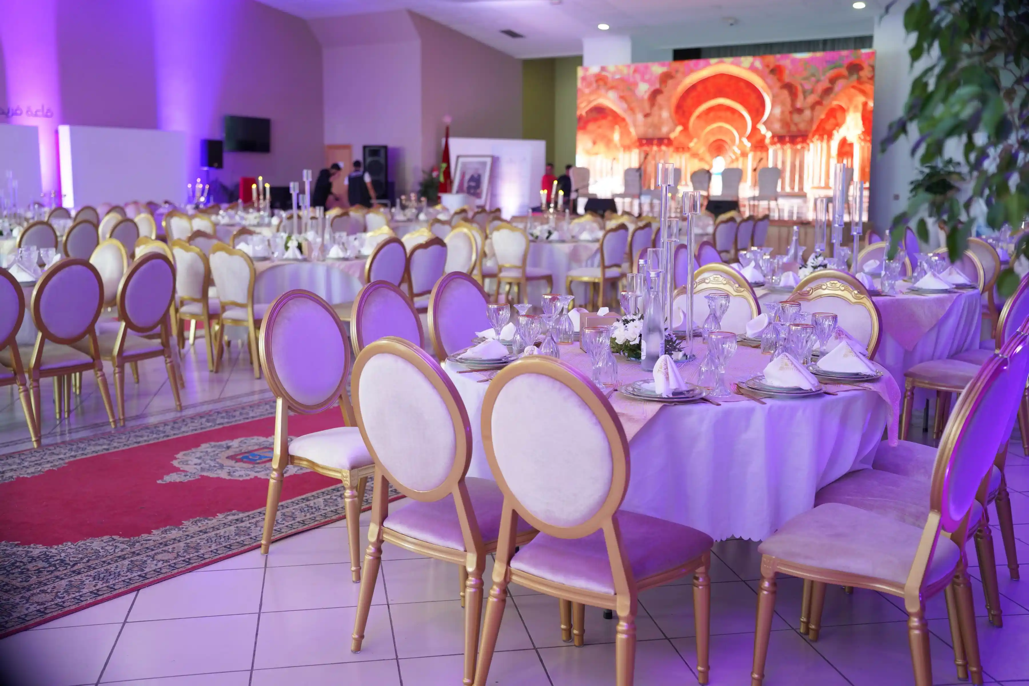 A banquet hall under violet wash lighting, tables laid and dance floor clear