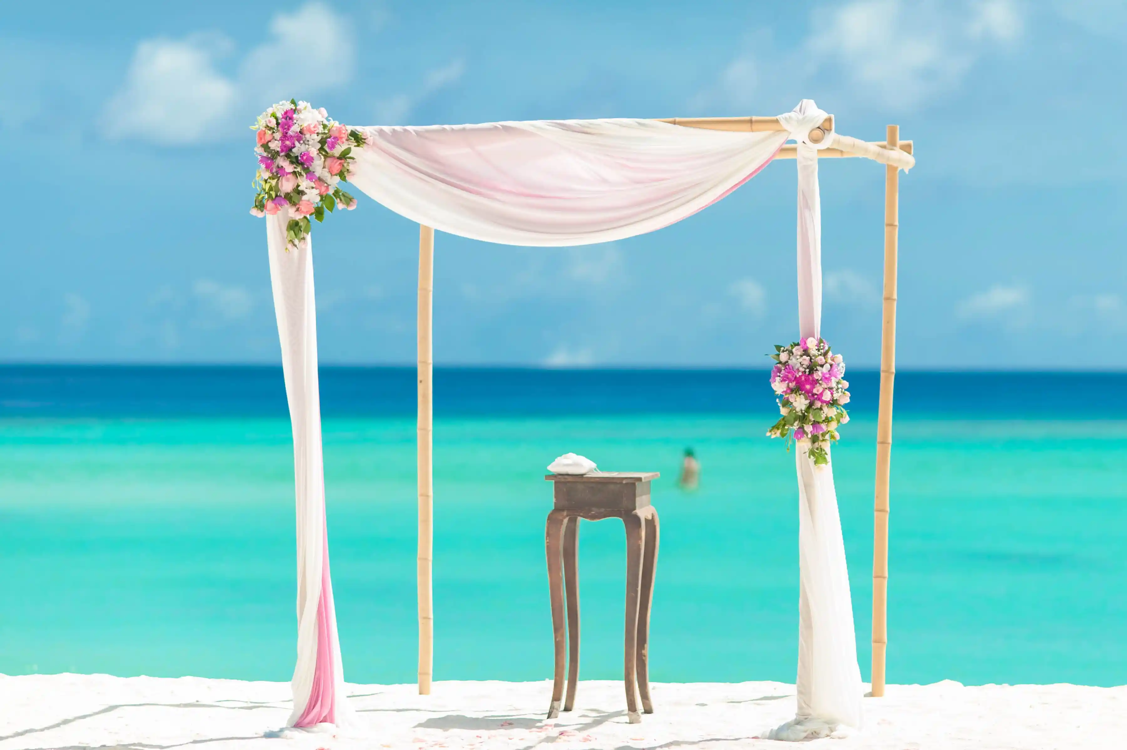 A draped wedding altar on white sand with turquoise water behind it