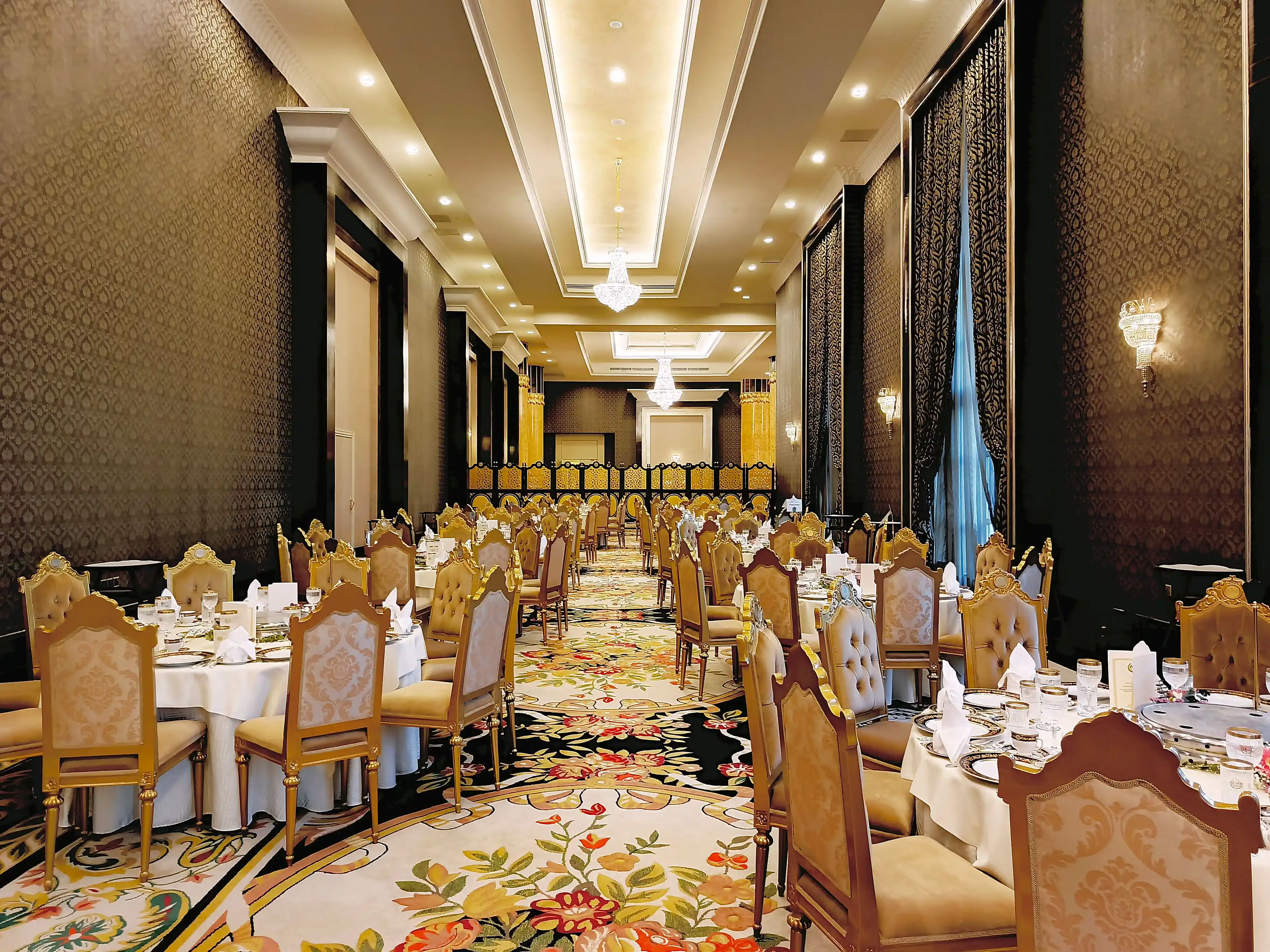 A hotel ballroom in warm gold light, round tables laid and a stage at the far end