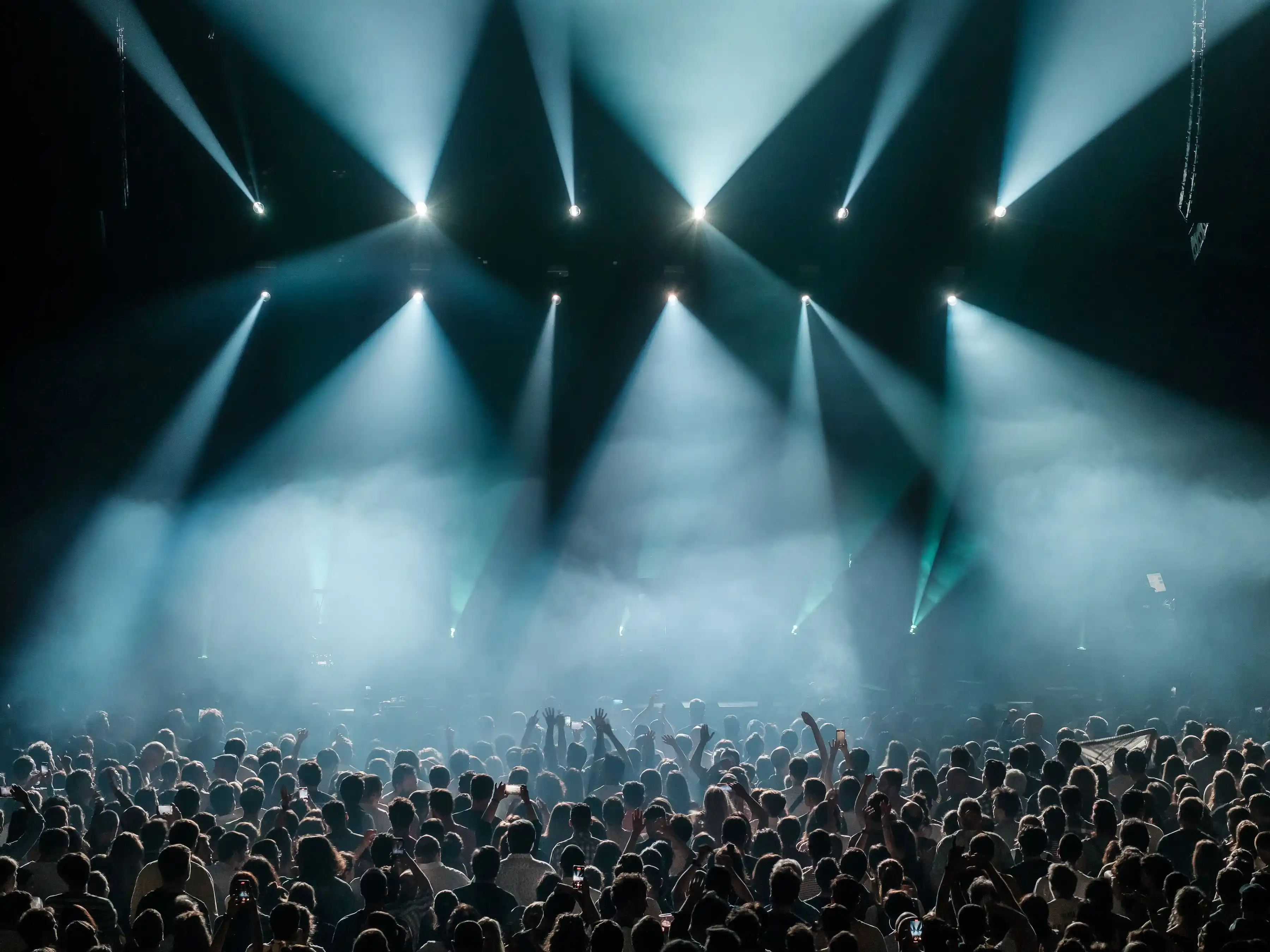 A dense festival crowd lit from the stage by wide beams of colour
