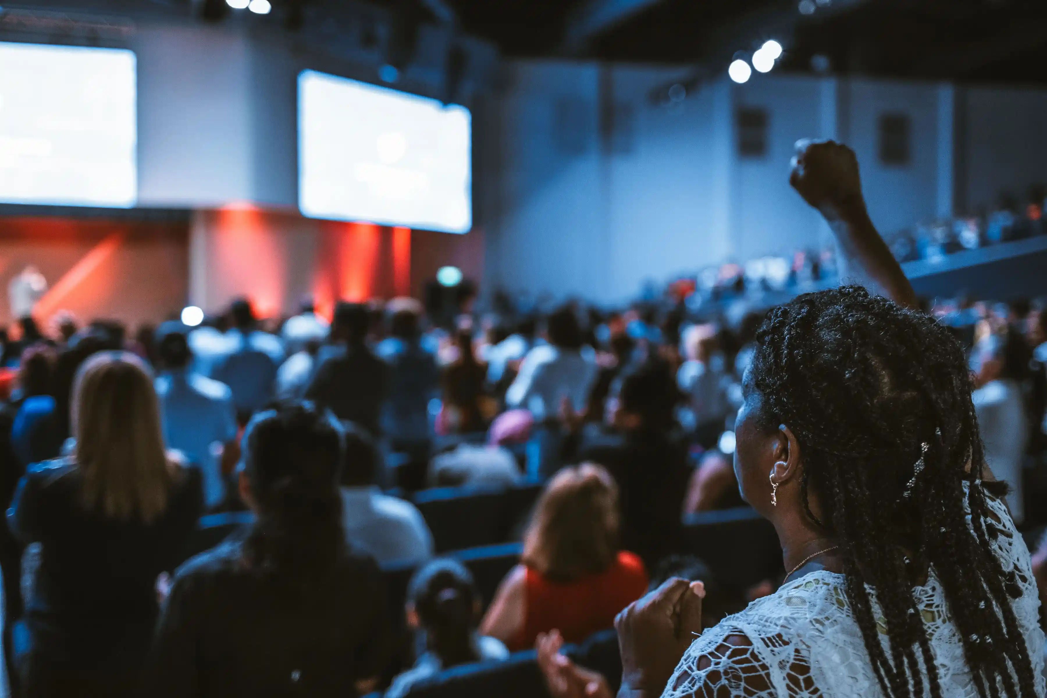 Delegates seated close together at a conference, one raising a hand