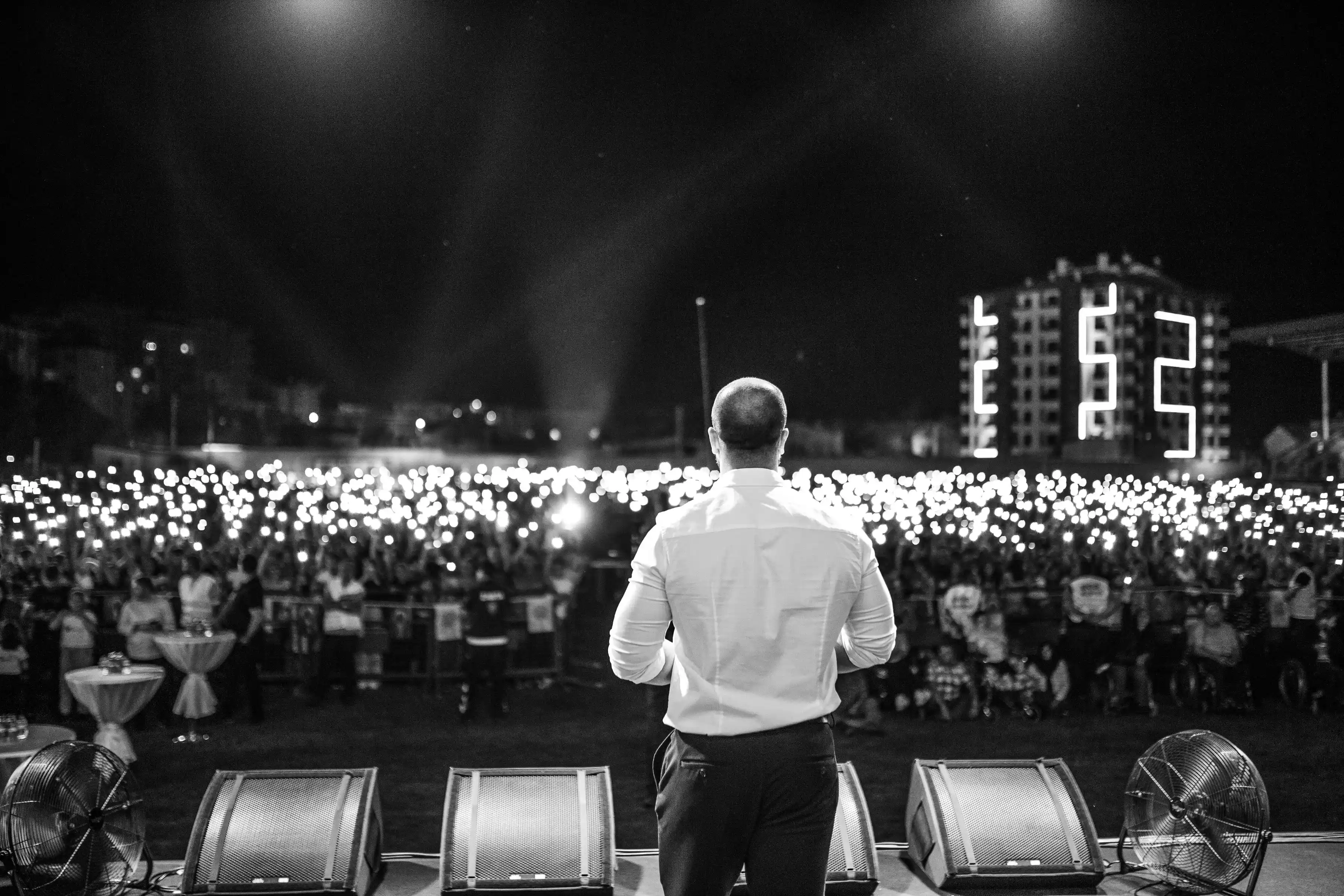 Black and white frame of a performer facing a crowd holding lights above their heads