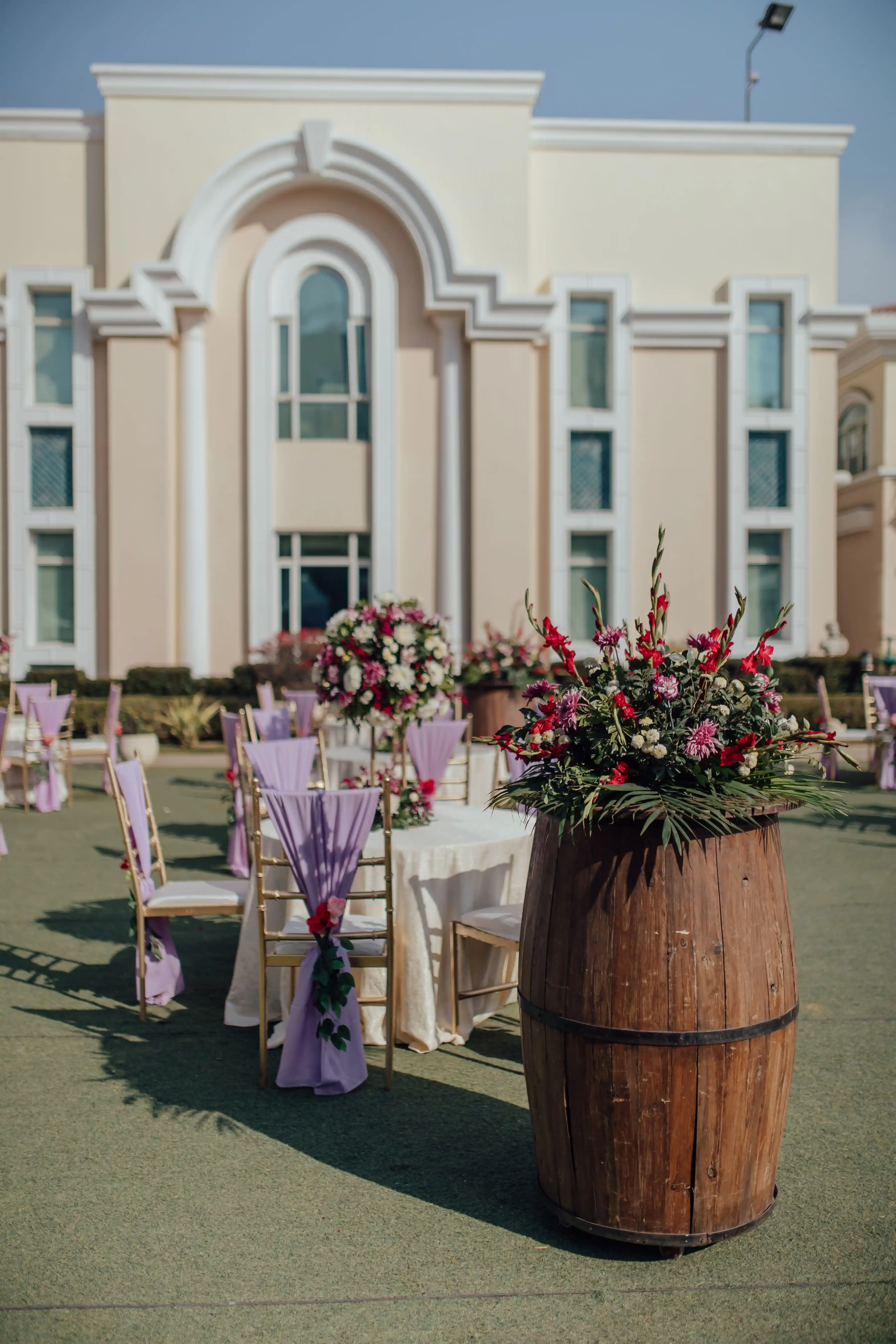 An outdoor wedding set on lawn in front of a pale colonial building, flowers on every table