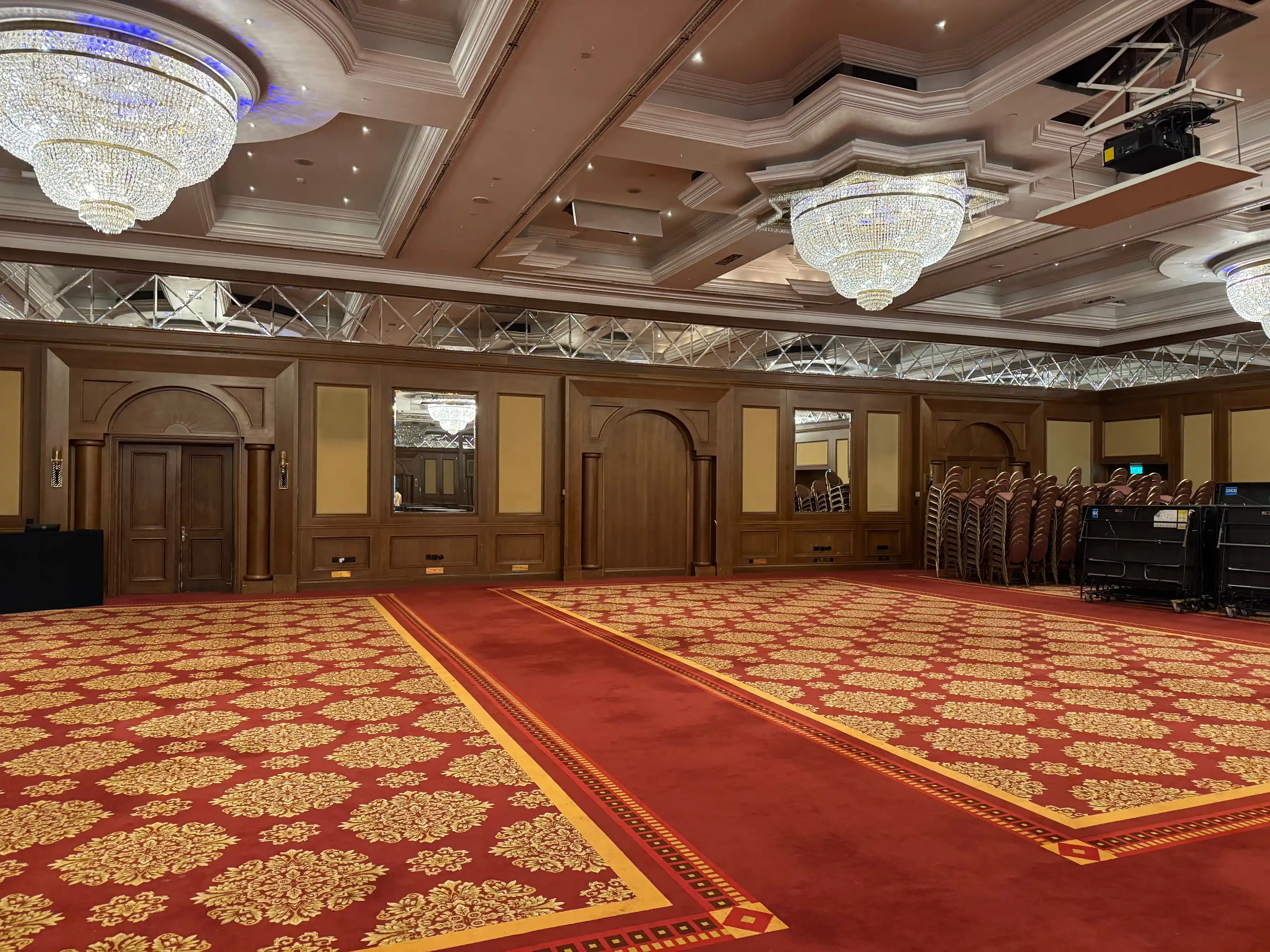 A banquet hall with chandeliers and a red carpet runner leading to the stage