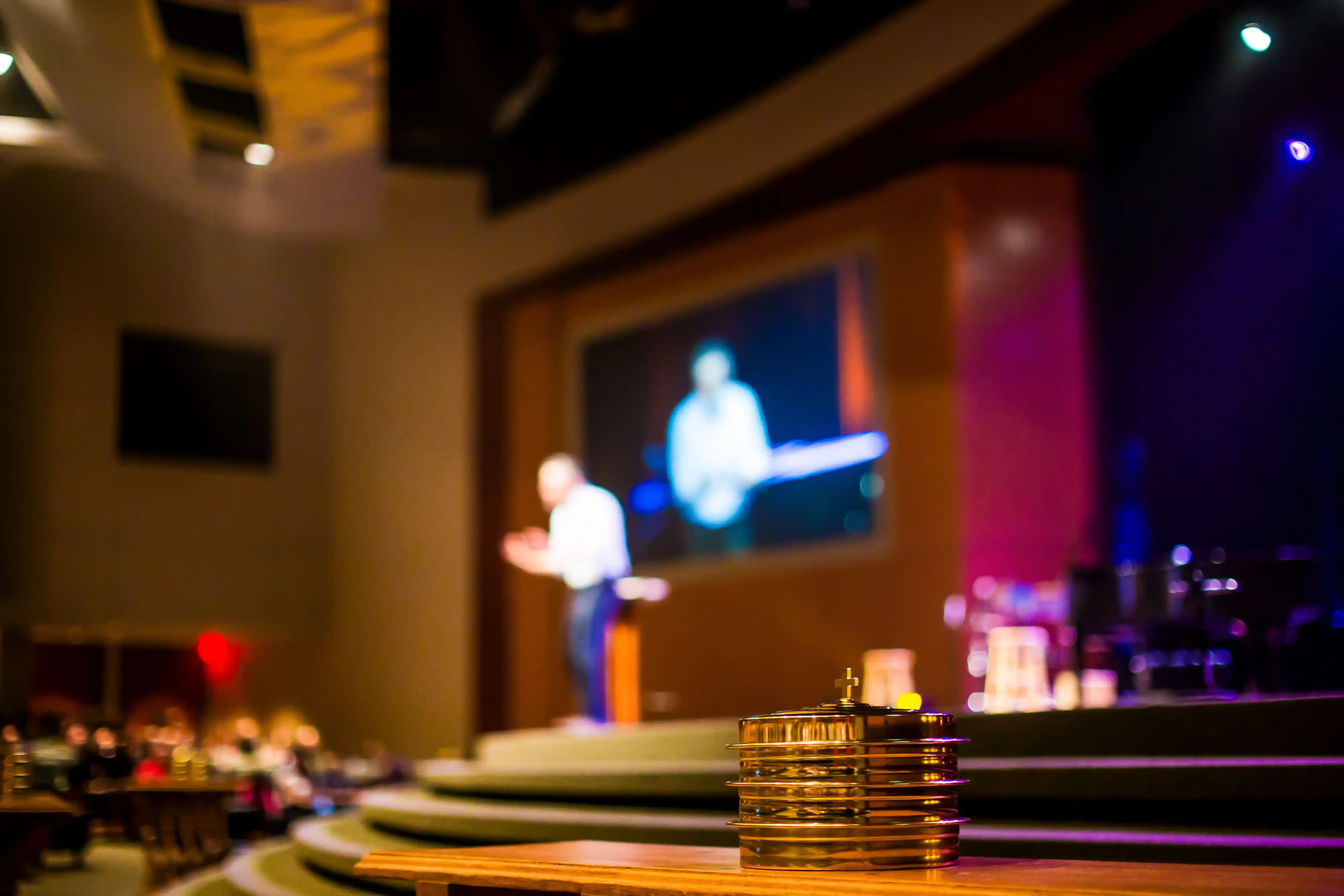 A microphone on a lit stage with a speaker out of focus behind it