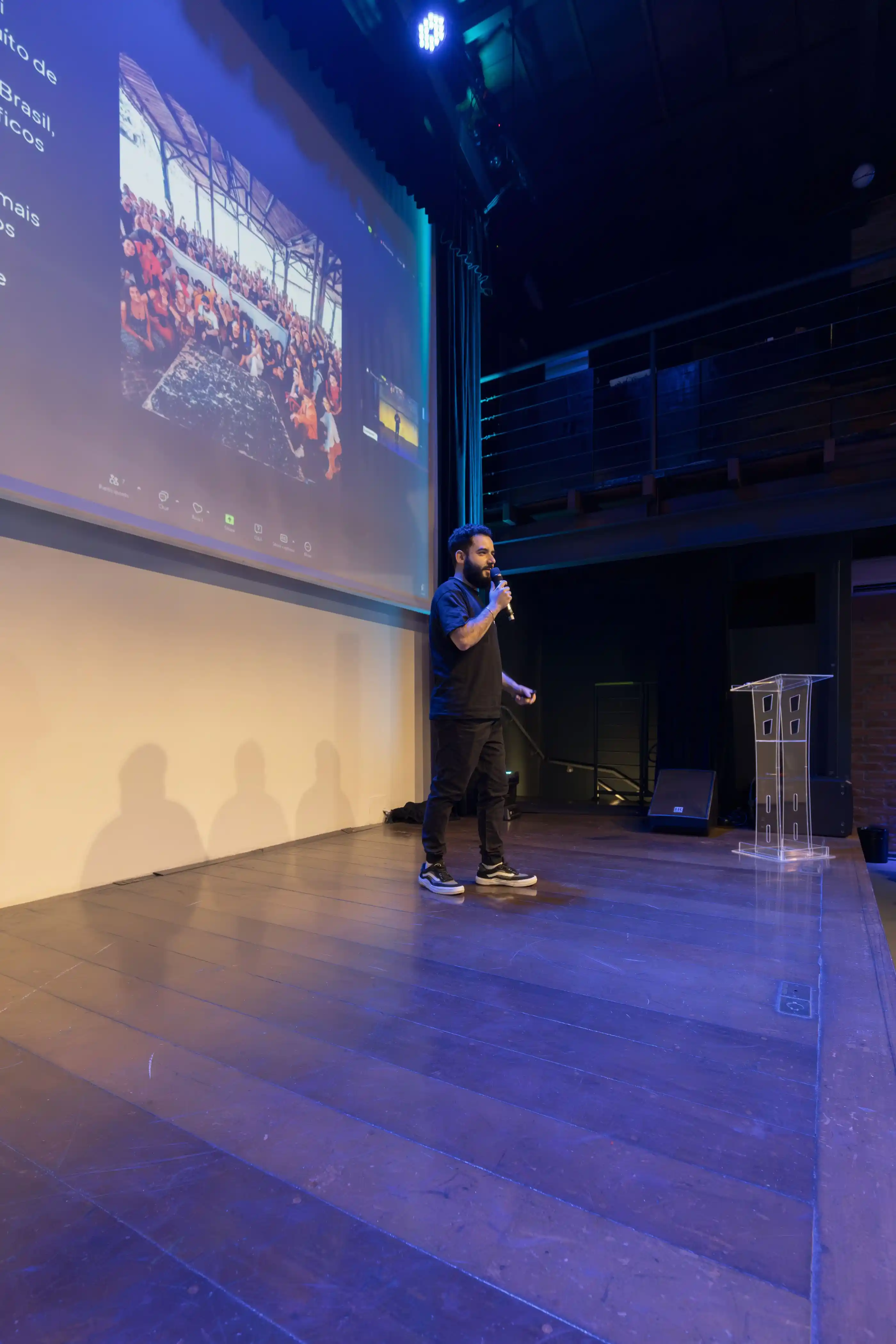 A presenter on stage in front of a large screen in a modern hall
