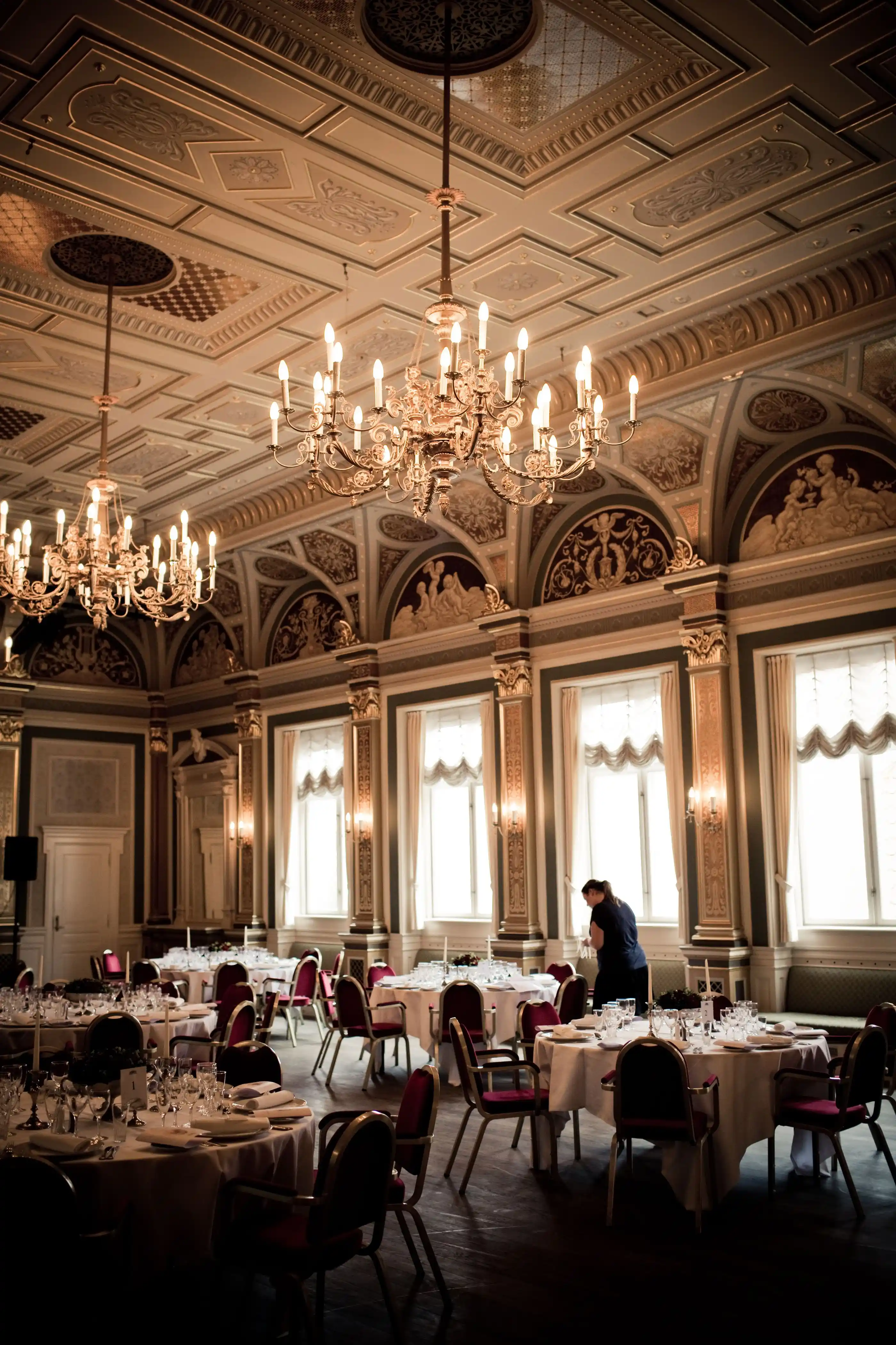 A classical dining room lit by chandeliers, ornate plasterwork overhead
