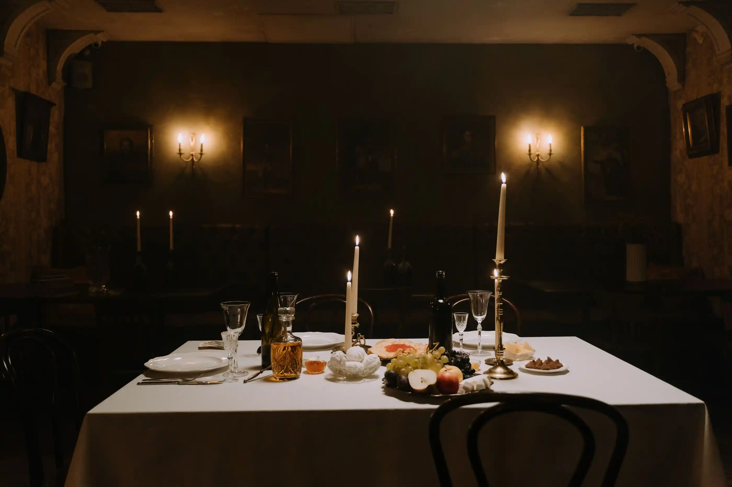 A dim dining room with a single table laid and candles burning