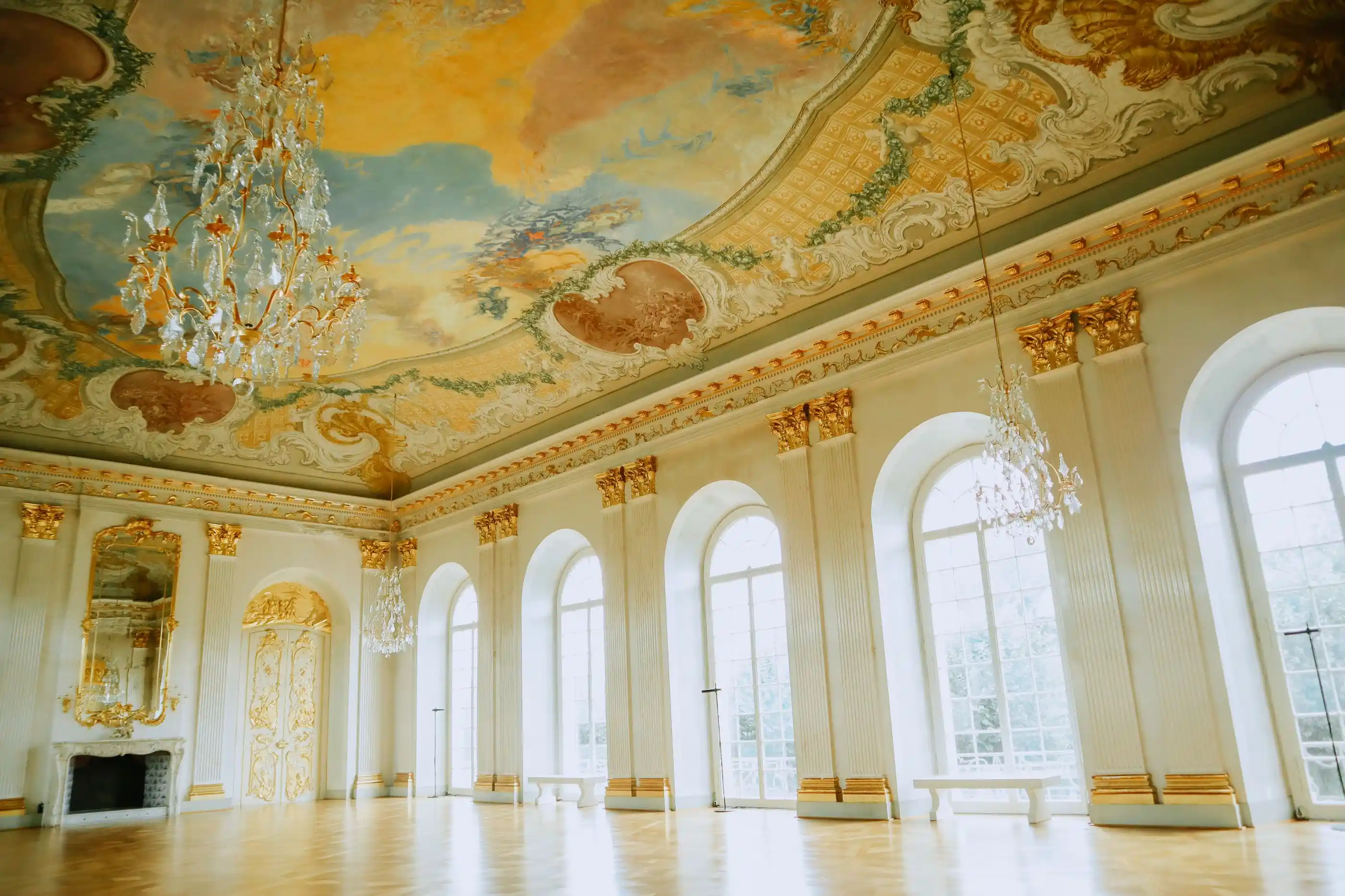 A ballroom with a grand chandelier and painted ceiling panels